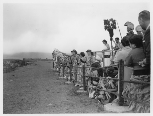 Black and white. A large group of people standing at the railing by the Halemaumau overlook