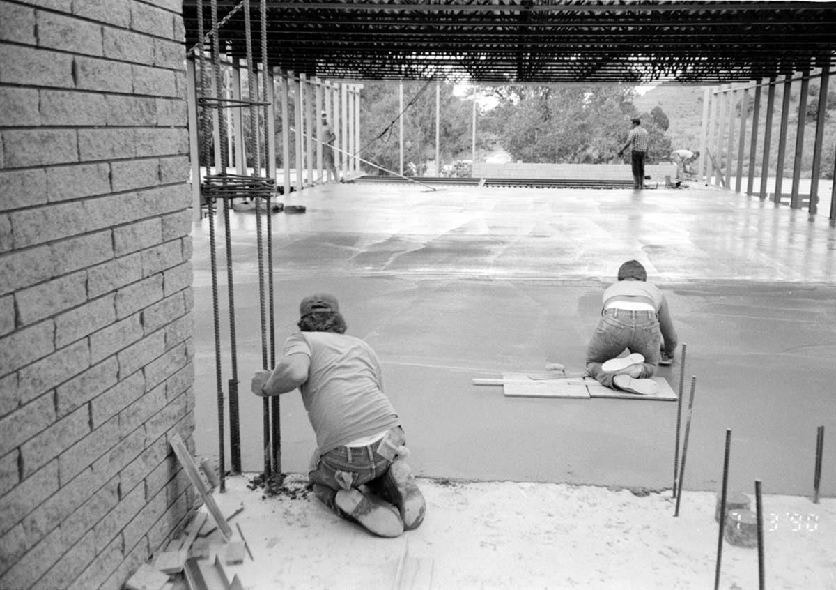Workers leveling cement in corner during construction of headquarters addition.