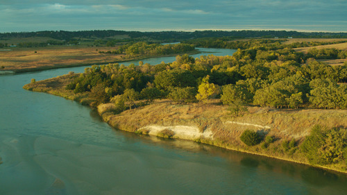 A winding blue river flows through low bluffs with trees and prairie alongside.