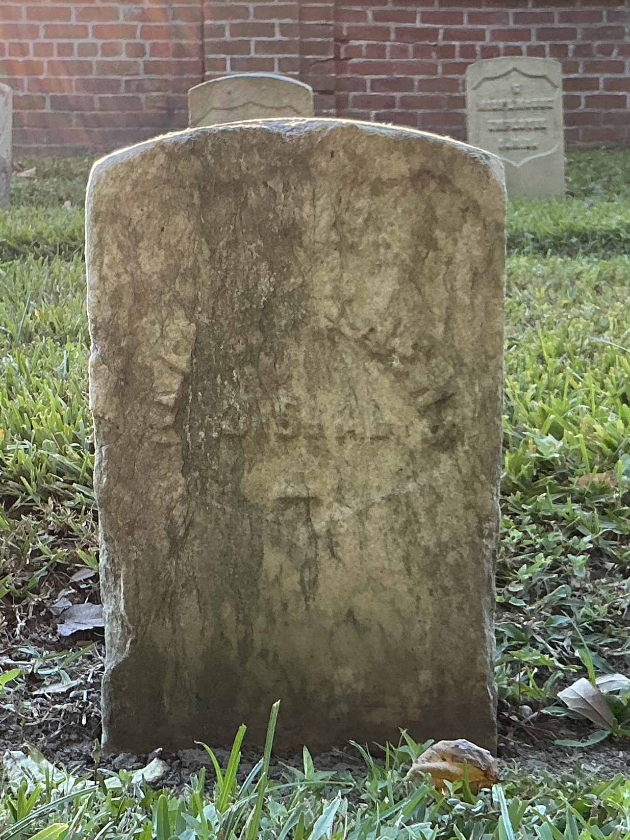 Front of historic upright marble headstone with recessed shield with recessed lettering face.