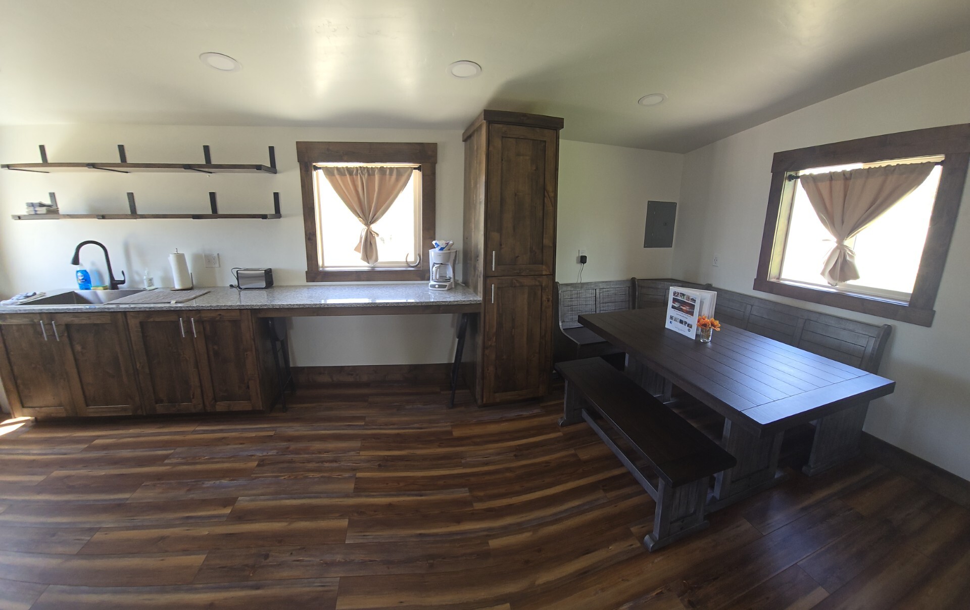 The bunkhouse has a rustic aesthetic with wood wall and ceiling paneling, a wood burning fireplace, kitchenette, and dining area.