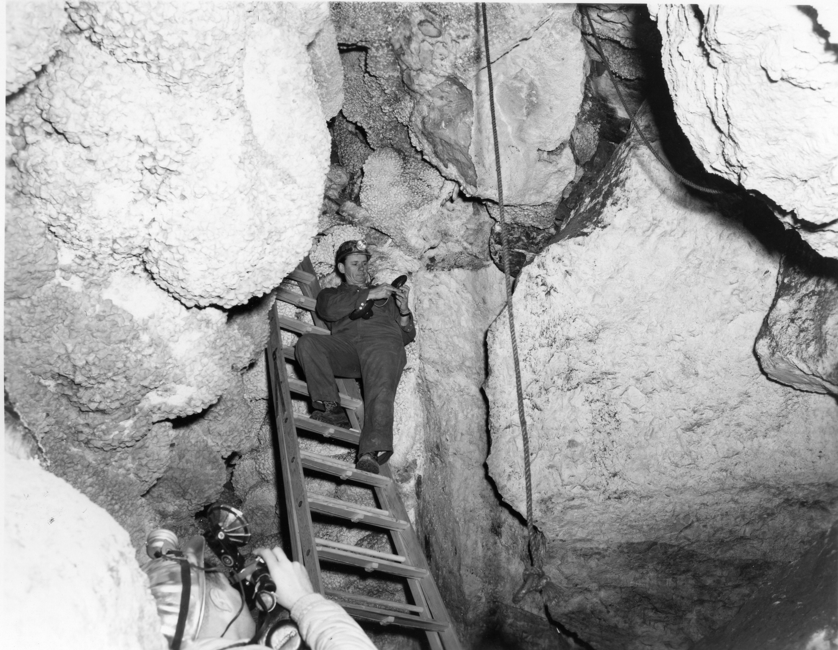 Man stands on ladder surrounded by rocks with rope hanging in center 