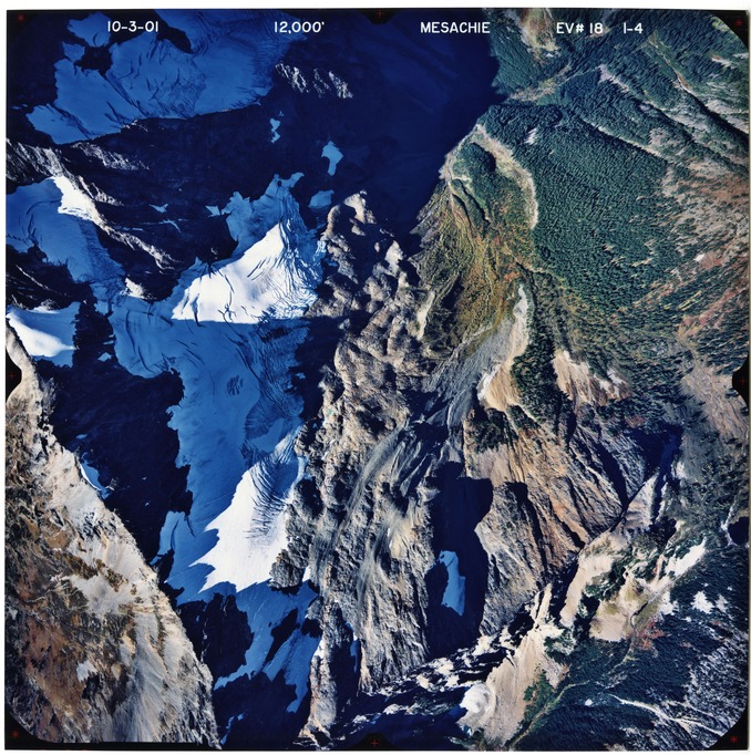 Color aerial photograph of glaciated mountain peak with forested valleys below.