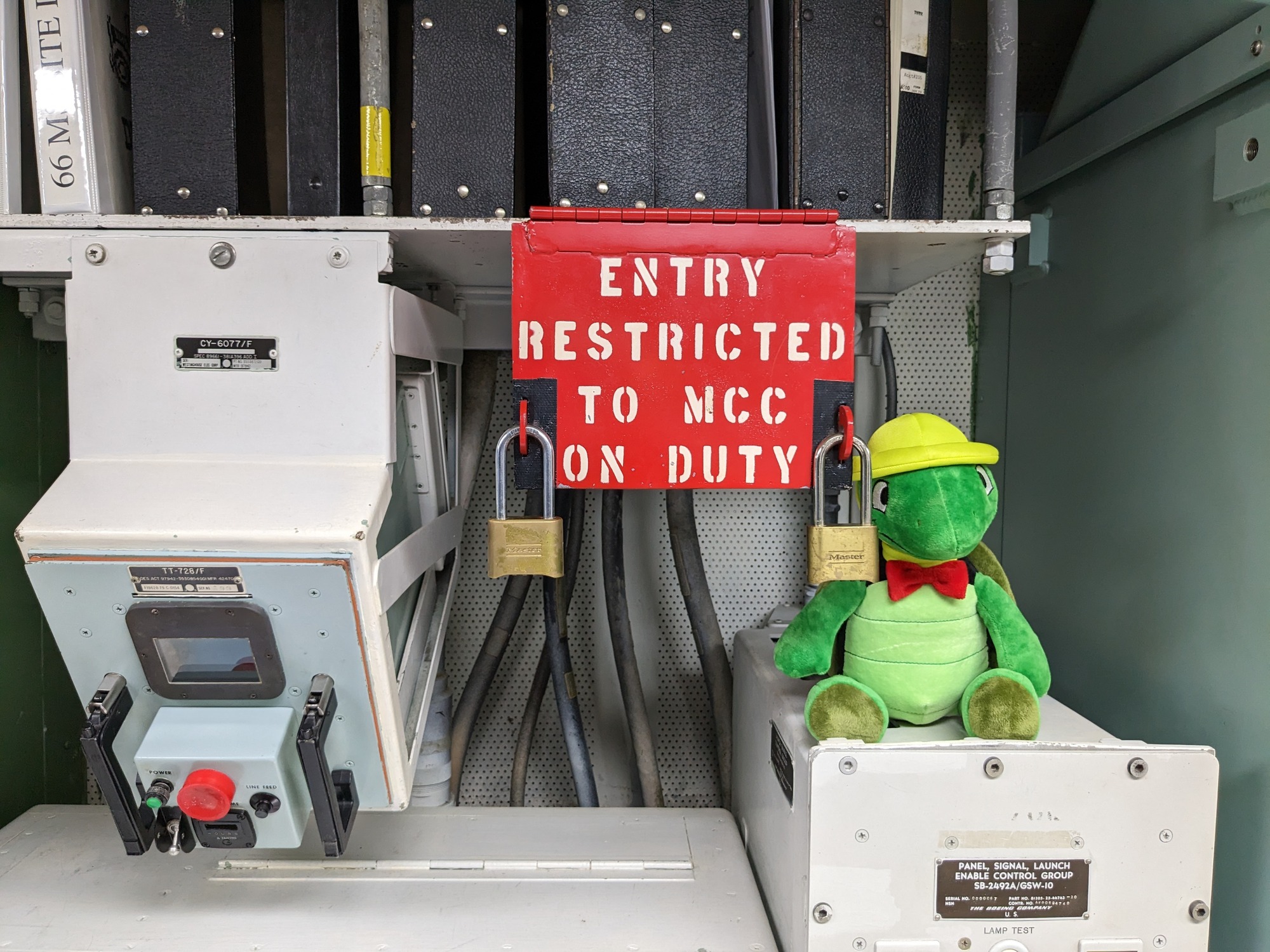 Plush green turtle sitting next to red box with padlocks that reads "Entry restricted to MCC on duty"