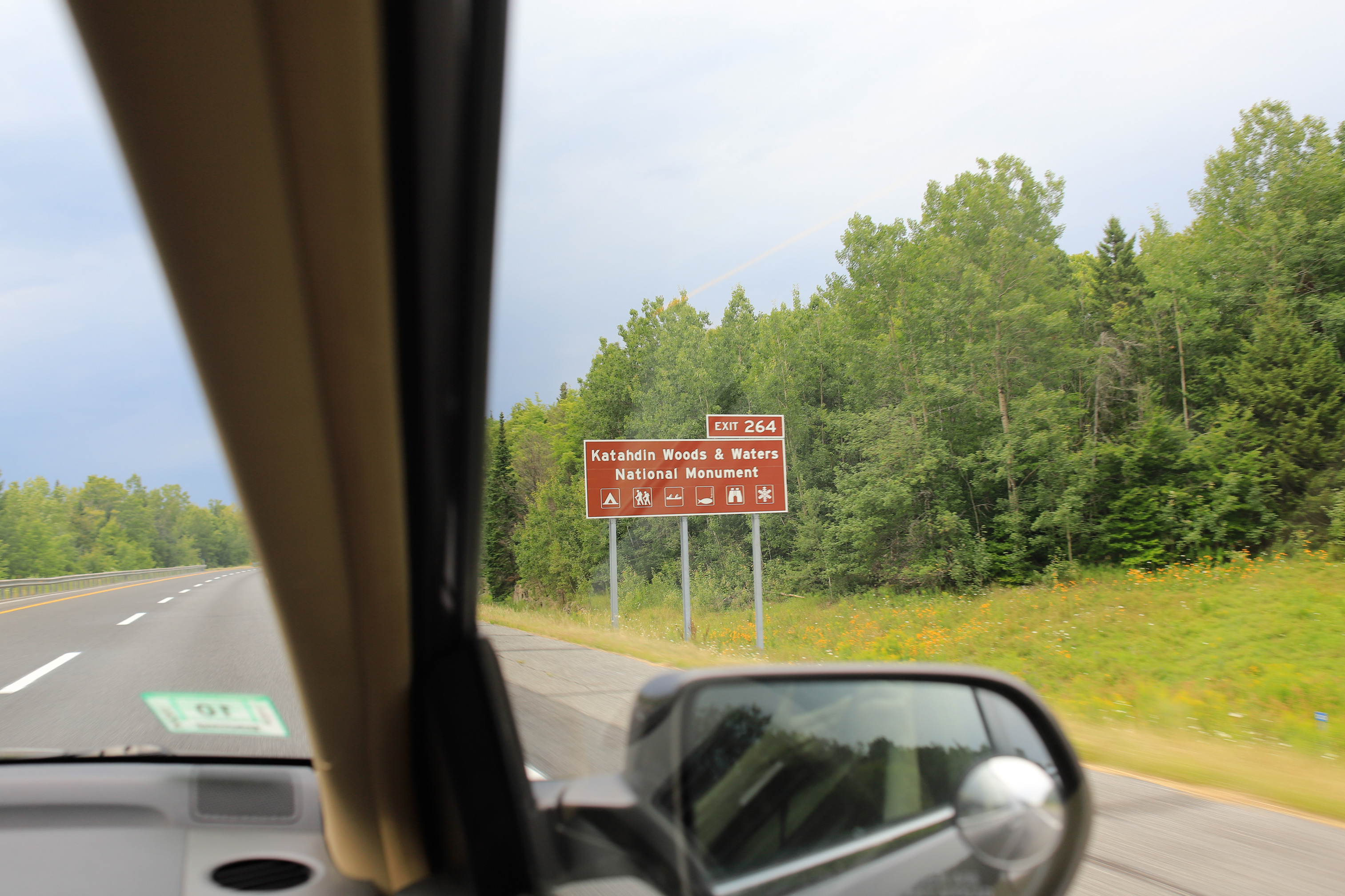 A highway exit sign for Katahdin Woods and Waters as seen through a passenger window