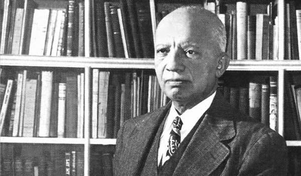 Historic photo of Carter G. Woodson in front of a bookshelf 