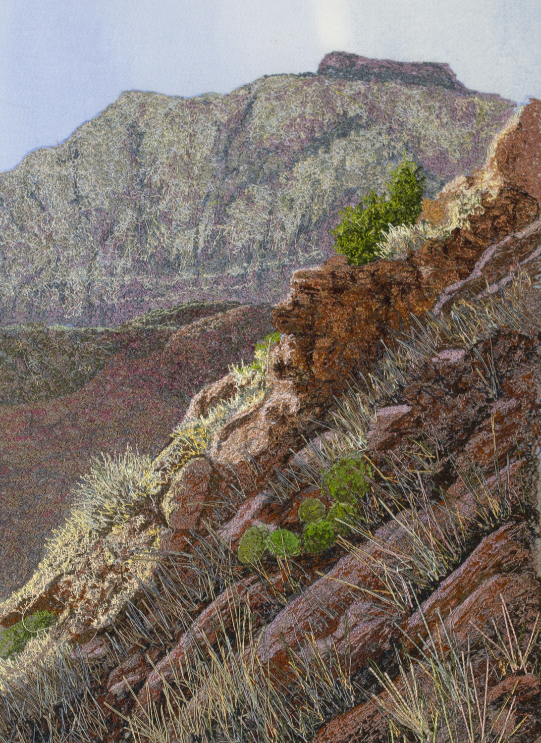 An image created using colored thread and fabric. This image shows a close view of a steep sandstone hillside. Various grasses, cacti, and small shrubs are nestled between large rocks. In the background, the tall sandstone cliffs of the "West Temple" are seen standing before a pale blue sky.
