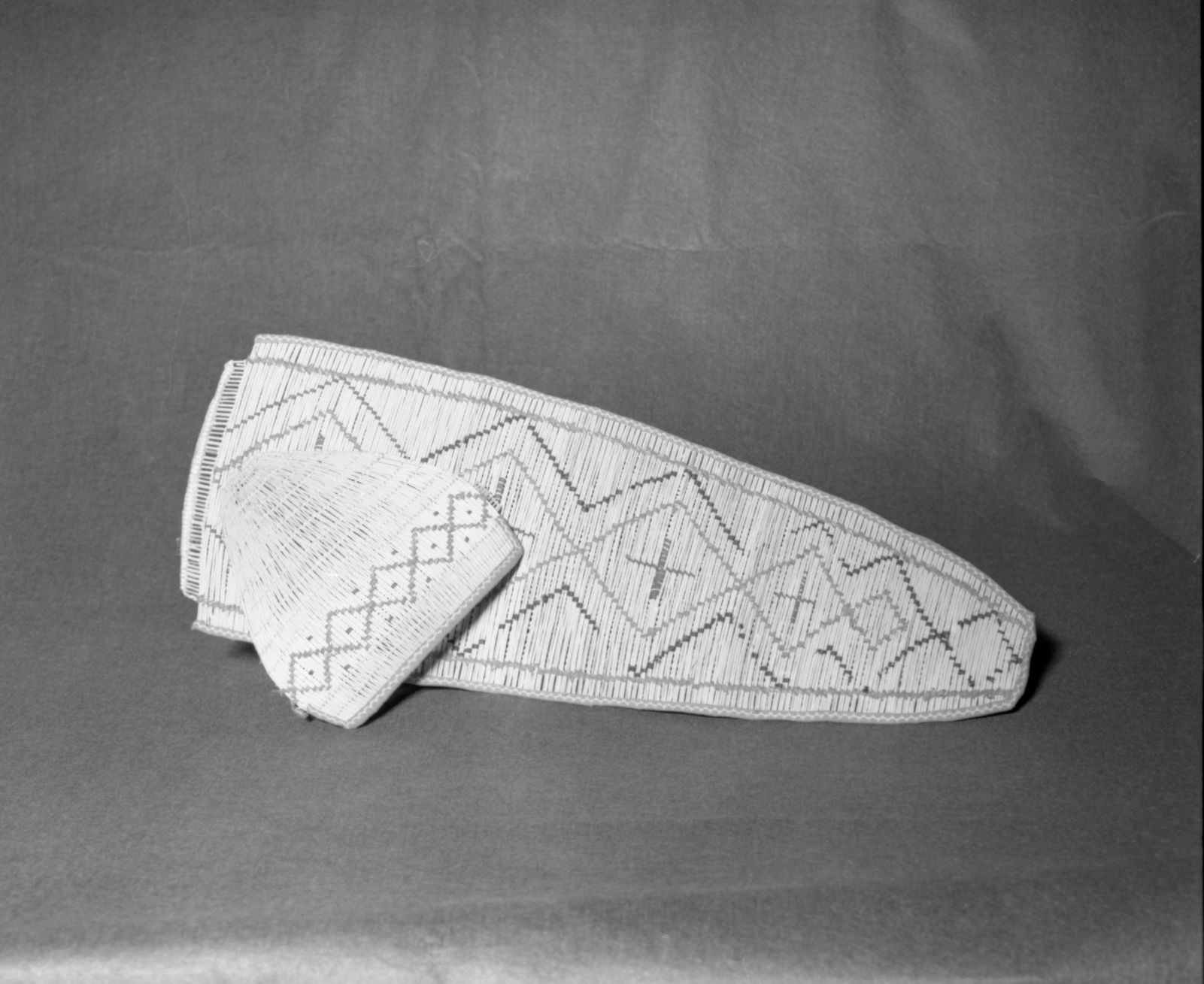 Mrs. Donald Segerstrom Collection. Object: Mono Lake or Owens Valley Paiute cradle. Dimensions: 25" length. Materials: Willow, red cloth, black thread. Technology: Horizontal and vertical planes bound with rags and string, vertical plane has 12 rows of plain twining in split willow shoots spaced equidistantly, hood twined in split willow diagonally, up to right slant of turns. Photographed by Michael Dixon. Catalogued by Craig Bates and Barbara Beroza. Yosemite Collections, National Park Service. 1/83.