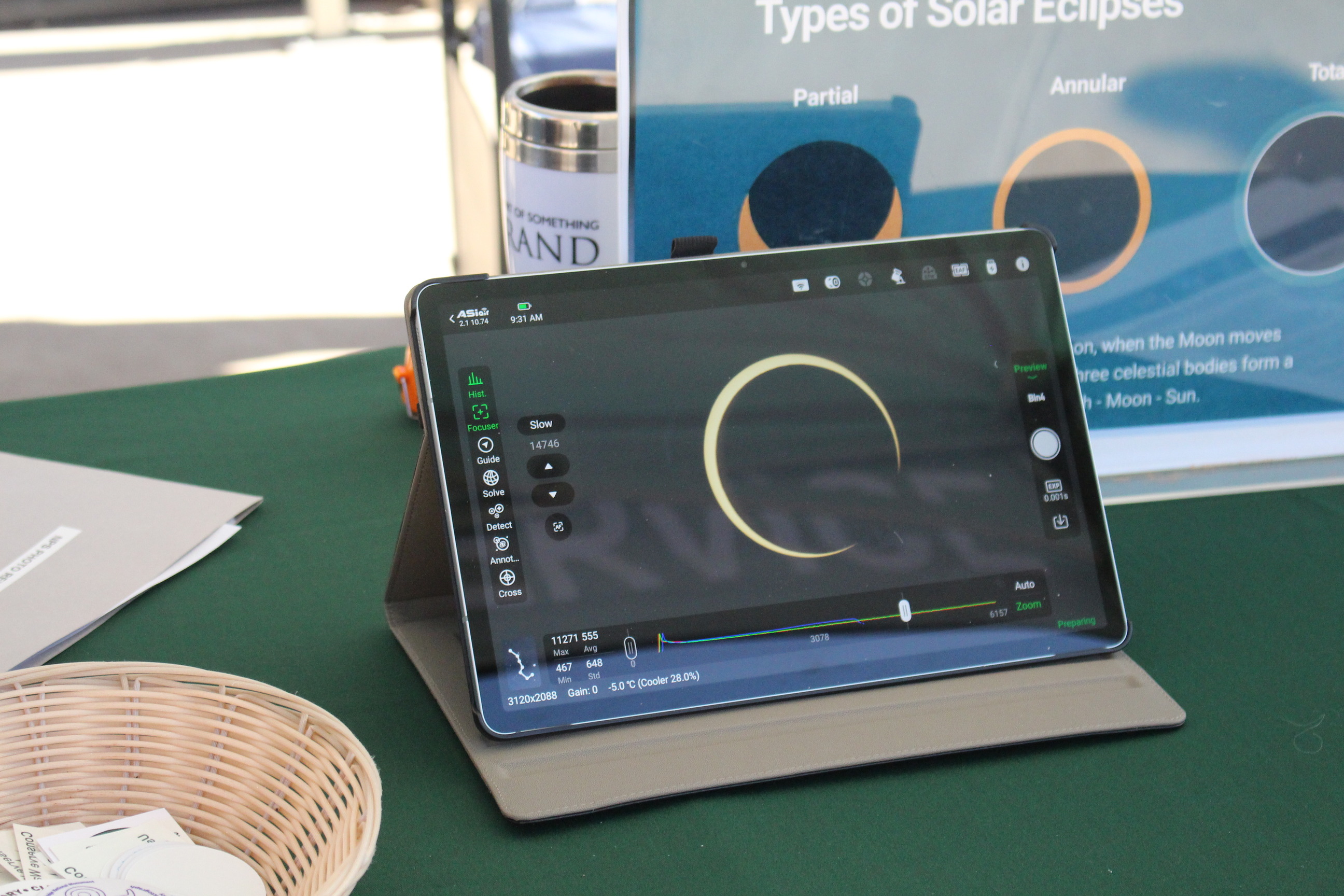 Tablet computer on a table. Image of partially eclipsed sun on the screen. Sign behind the tablet indicates types of eclipses.