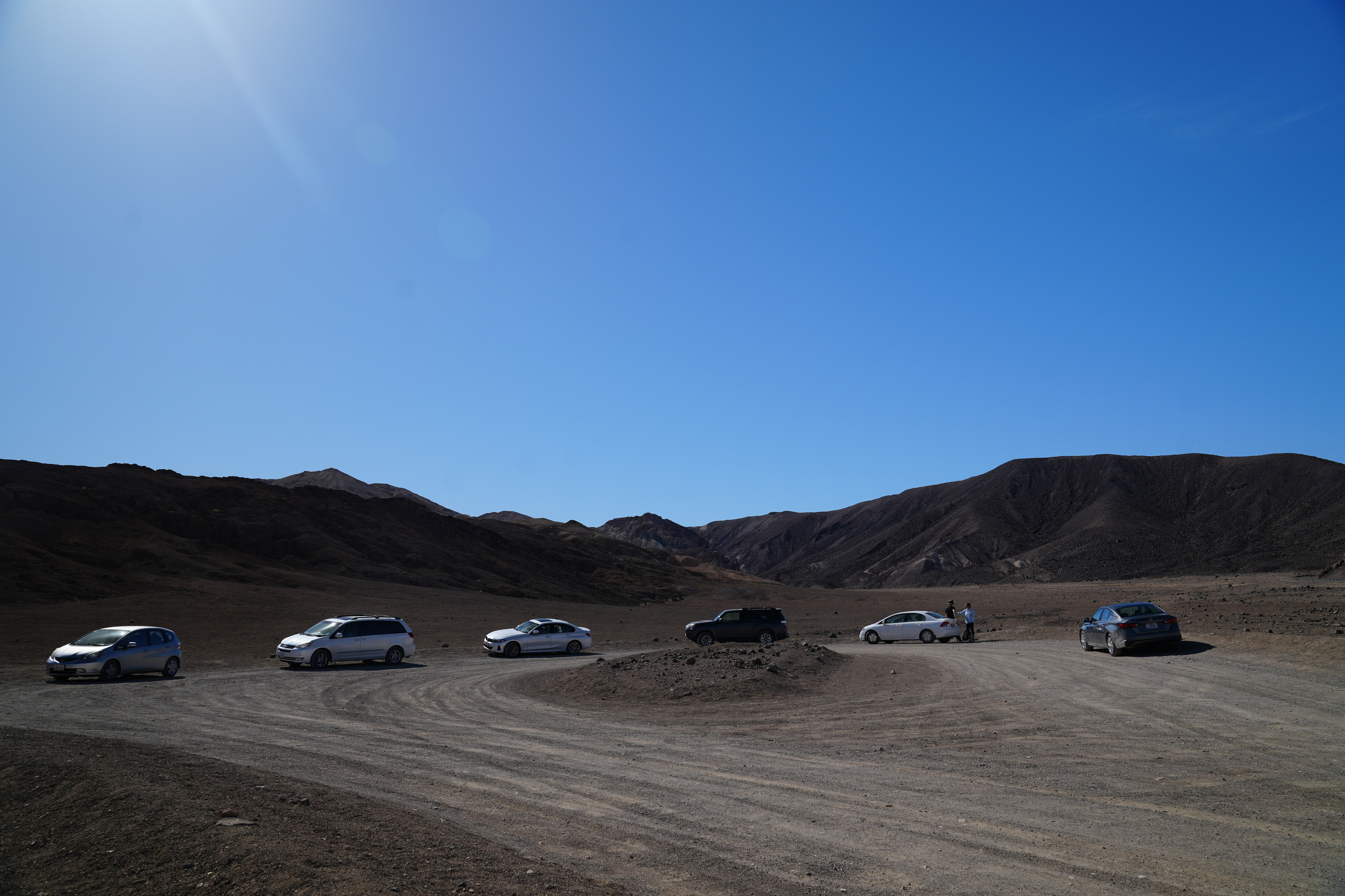 Desolation Canyon parking. The parking lot is largely gravel with a round-about structure. There are no other signs of infrastructure other than the gravel lot that is cleared amongst, natural gravel alluvium. There are cars parked along the dirt clearing. A mountain can be seen in the background