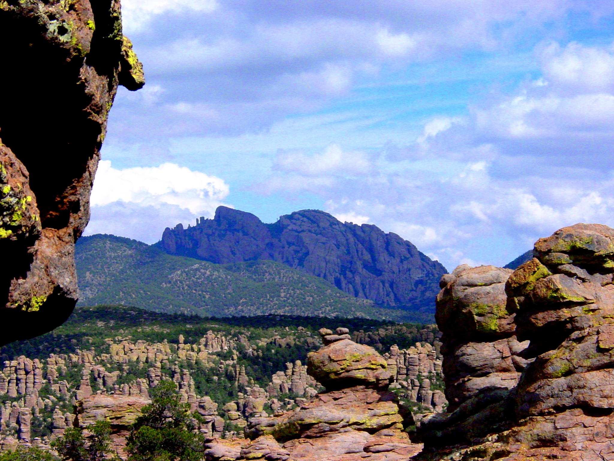 Rock pinnacles with a view of a mountain that has a face-like profile (chin, lips, nose, forehead) in the background. 