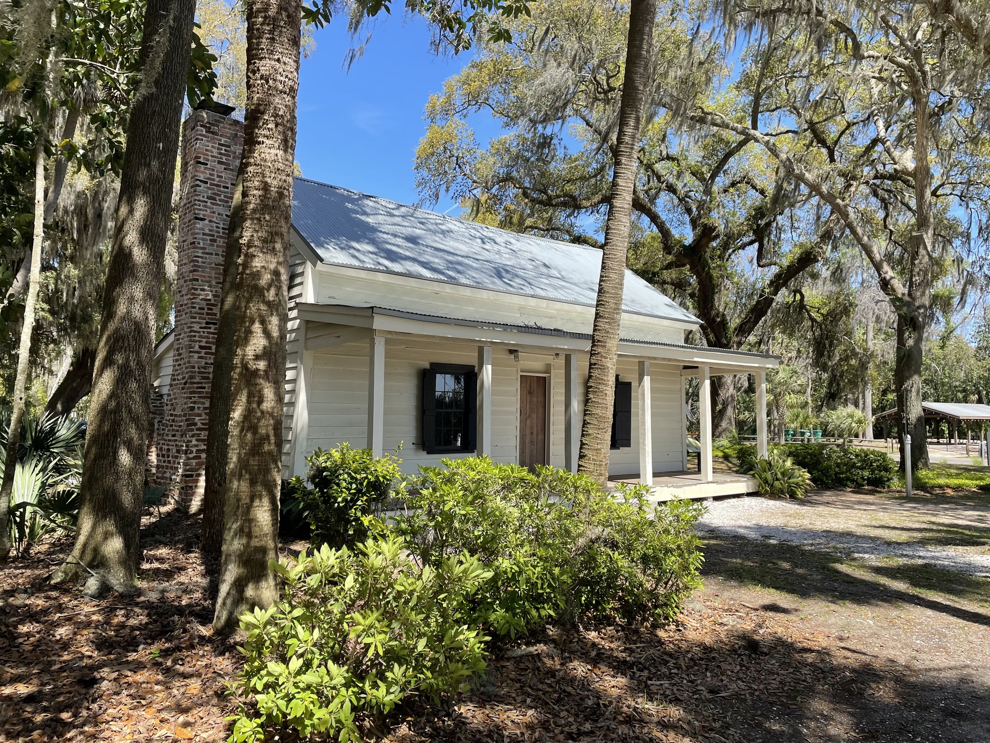 A small white house with a porch set in between trees.