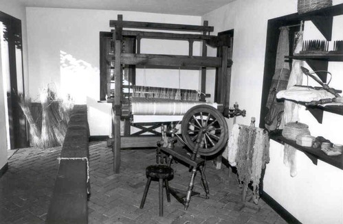 Historic image of the interior of the weaving and spinning shop with loom and spinning wheel