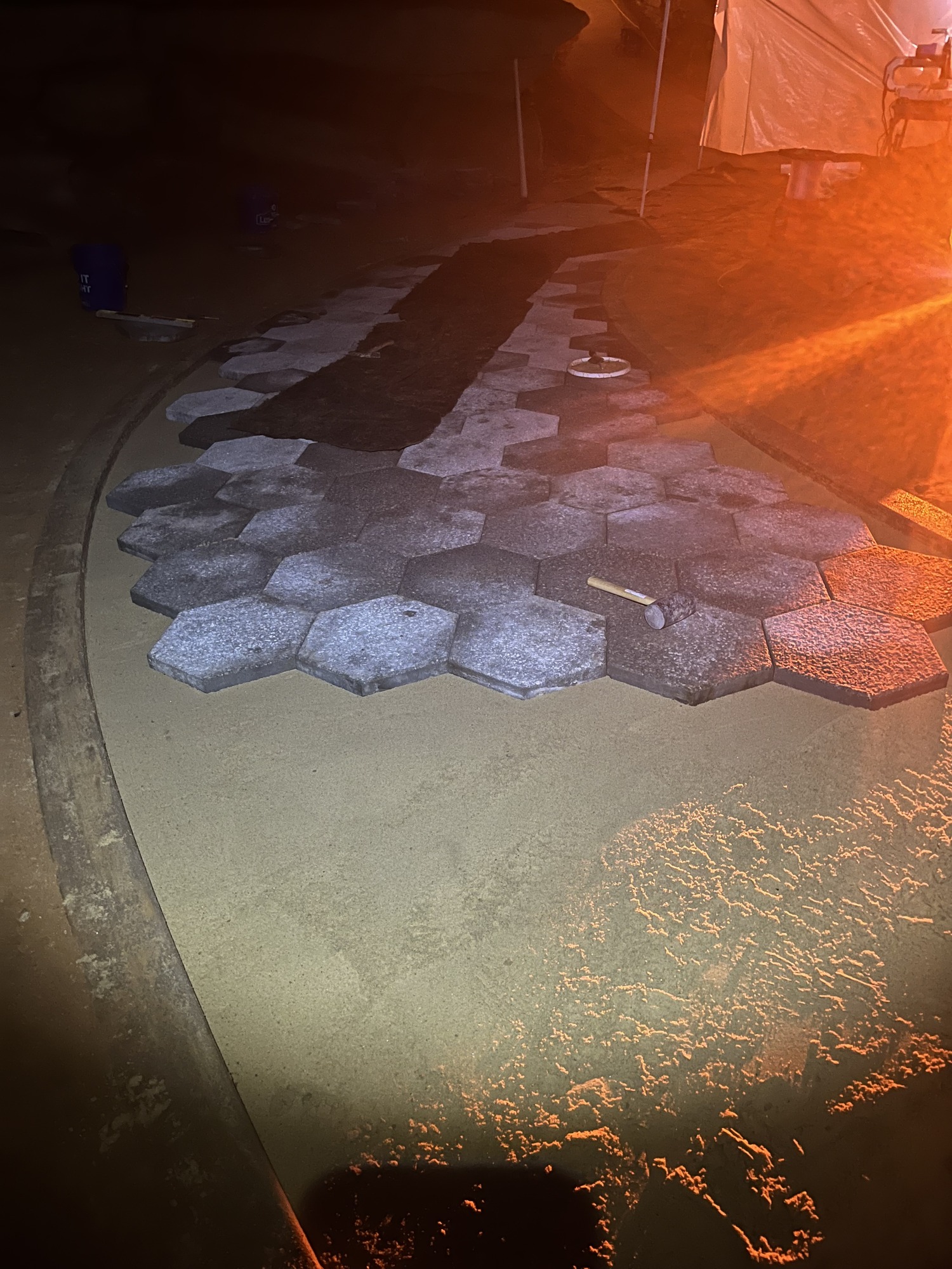 A row of hexagon shaped concrete paving stones are laid in a pattern on a sandy floor.