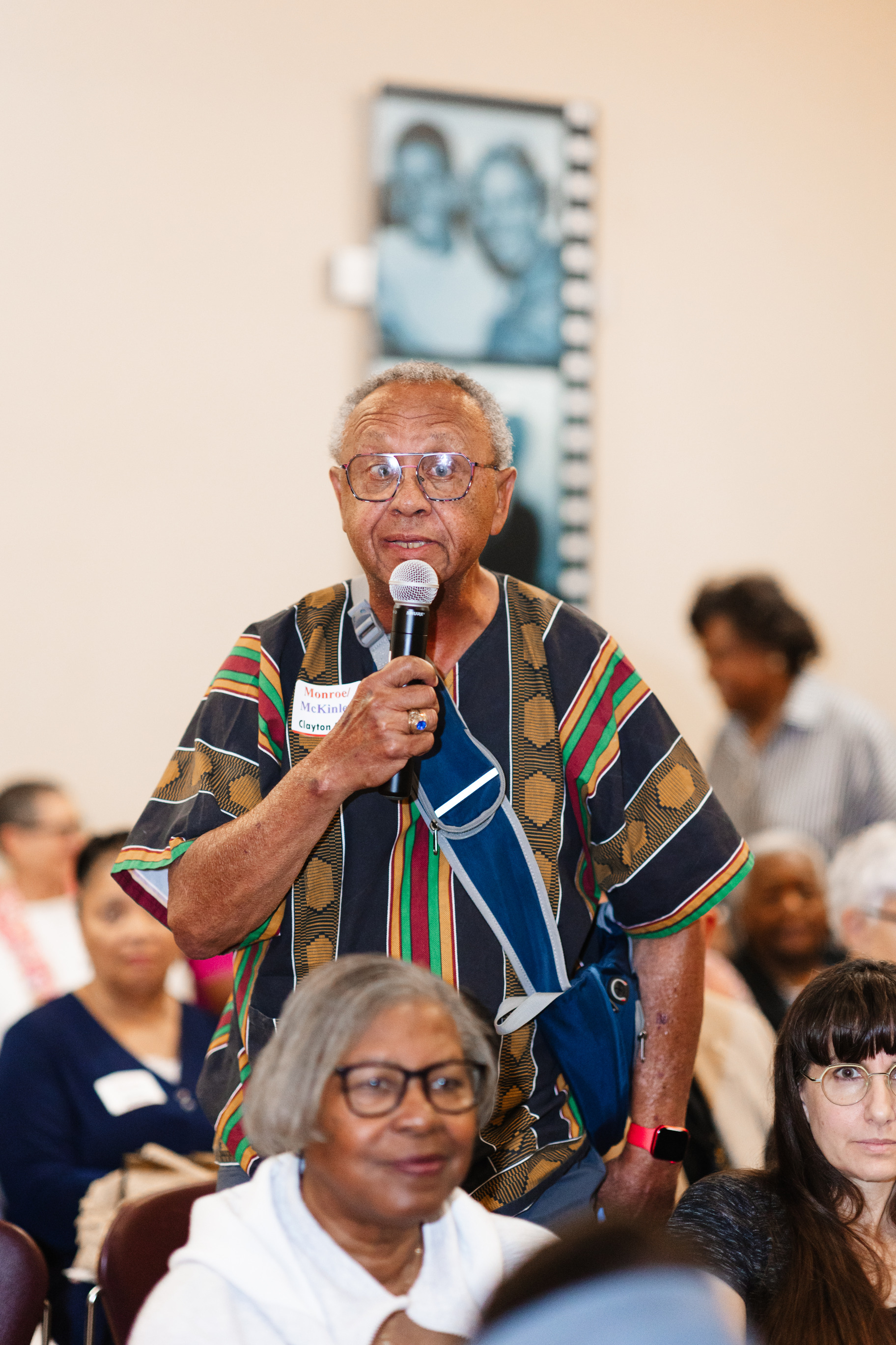A close up shot of an adult African American man standing in a crowd holding a microphone in his hand. He is in the auditorium of Brown v. Board of Education NHP.