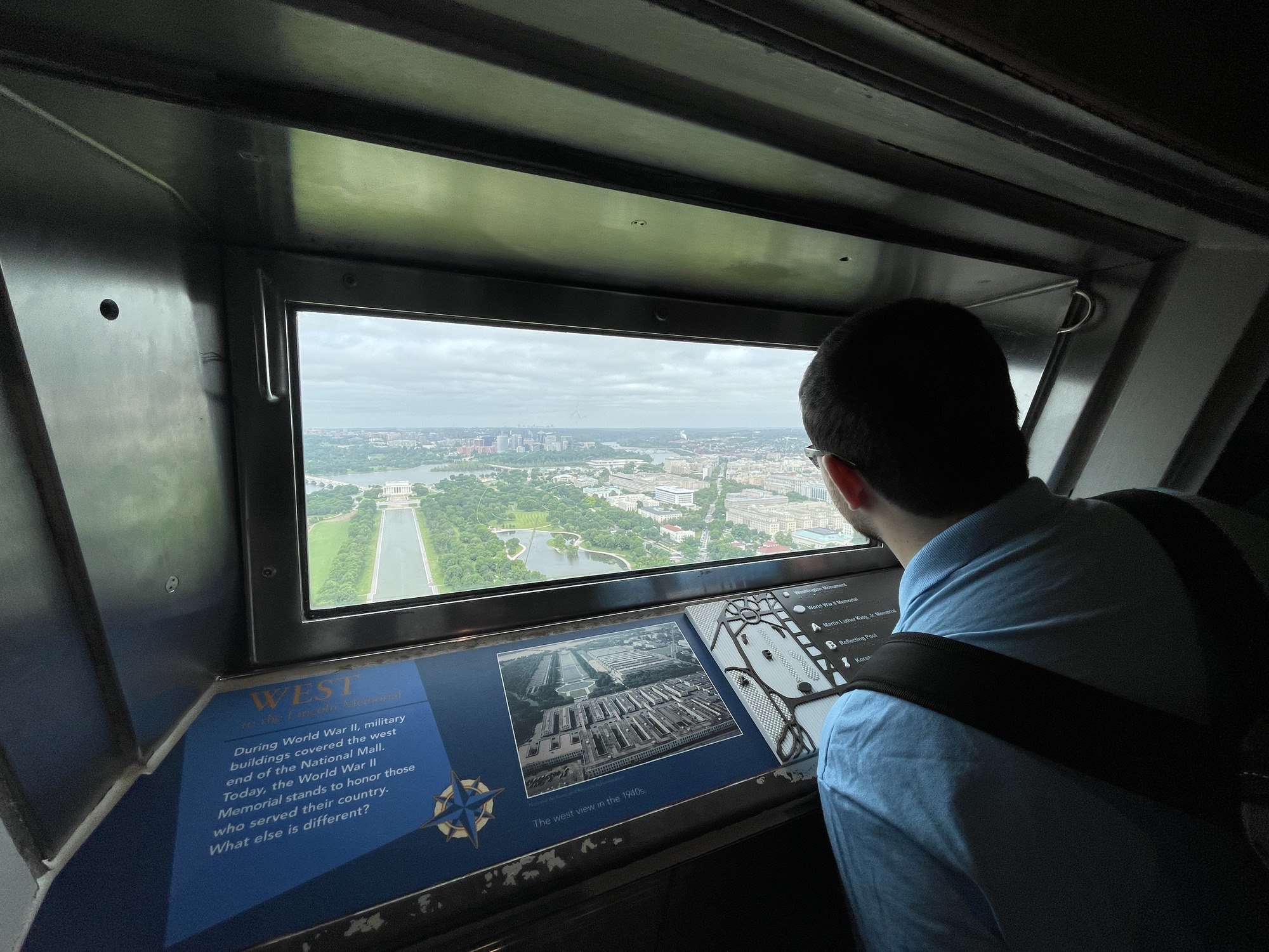 Man staring out a window with the faraway view of the Lincoln Memorial, trees, lakes and houses.