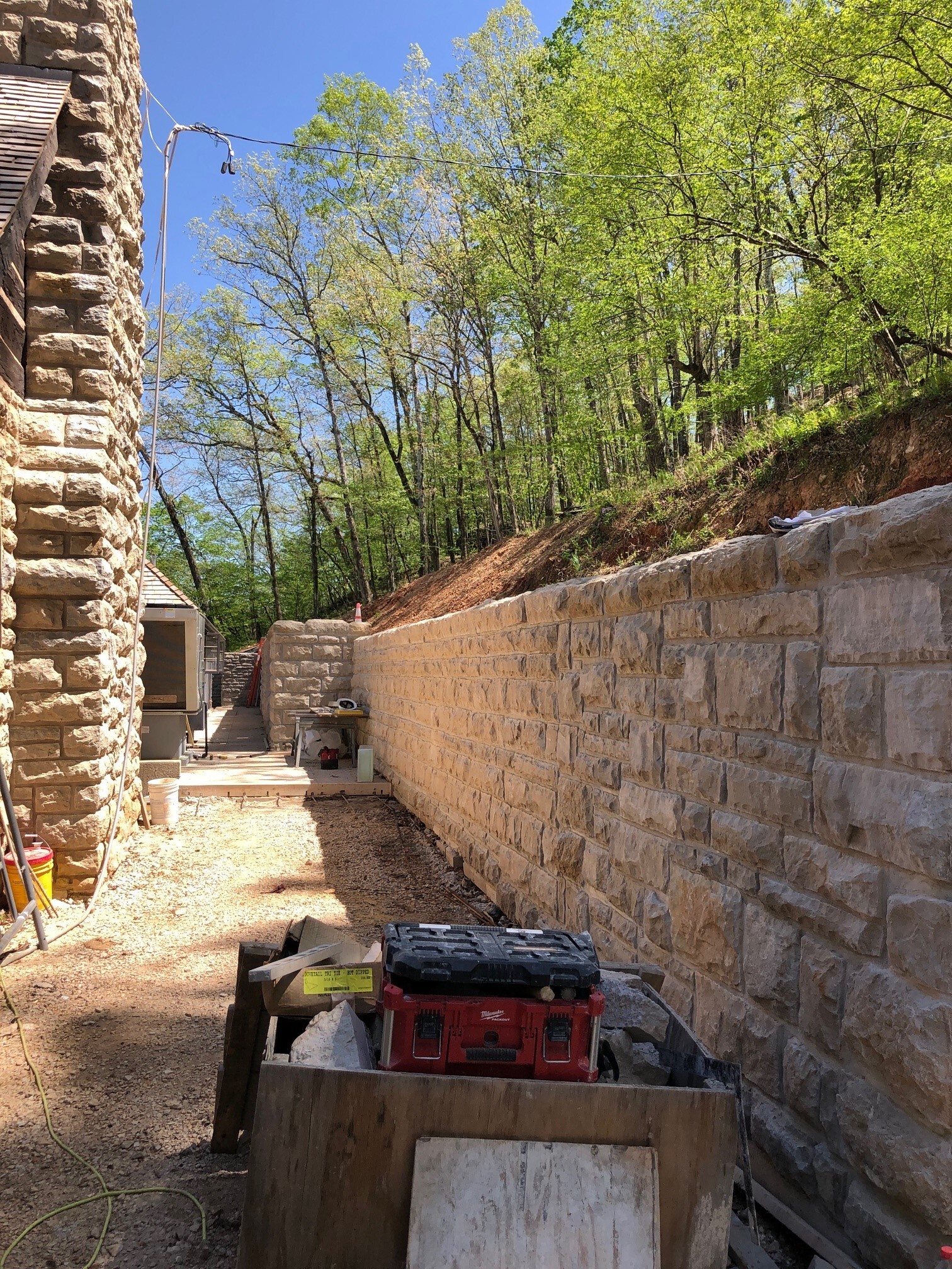 A rustic stone wall, with green trees on the hill above.