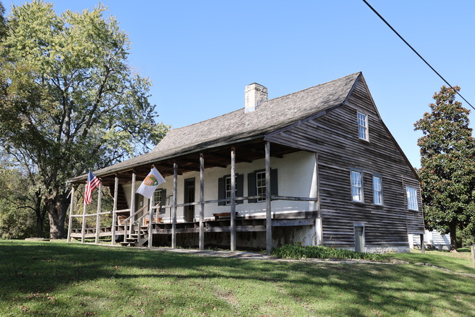 A house with a covered front porch, white front, plain wood siding and shingles.