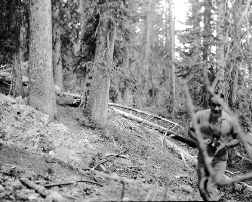 Man with camera standing next to water supply hose on forest floor. Record of water exploration.