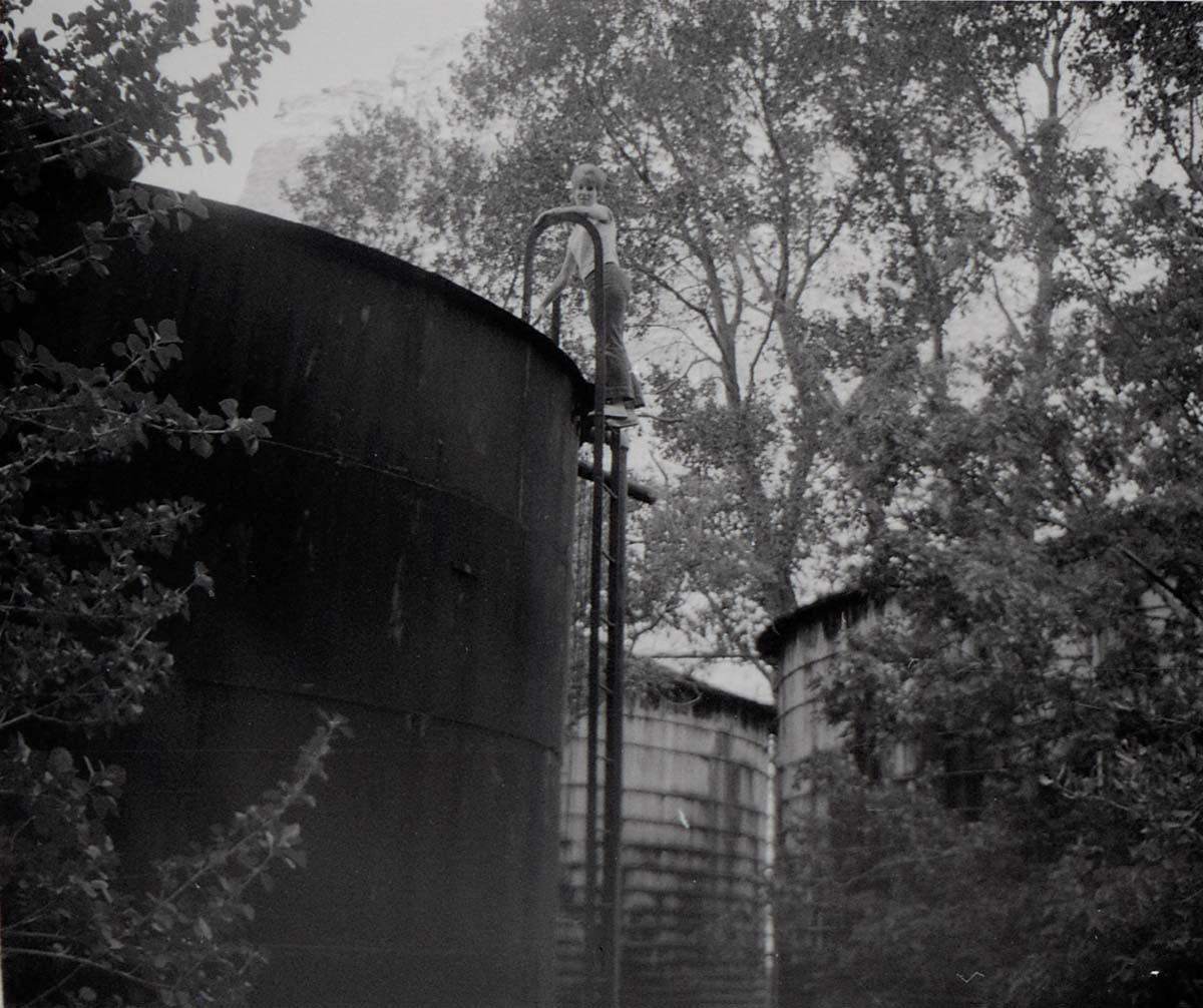 Woman standing at top of water tank ladder prior to start of reroofing project.