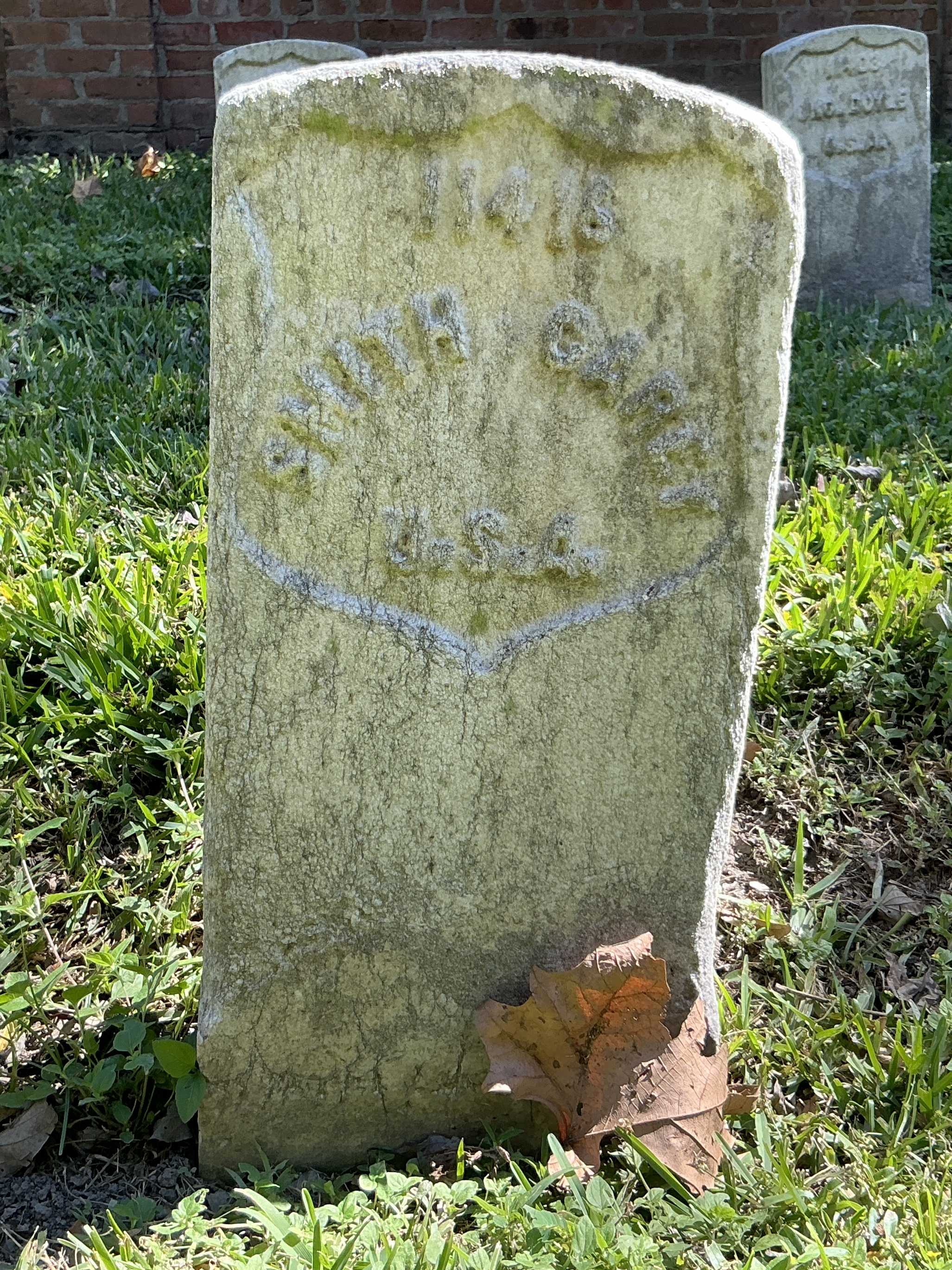 Front of historic upright marble headstone with recessed shield with recessed lettering face.