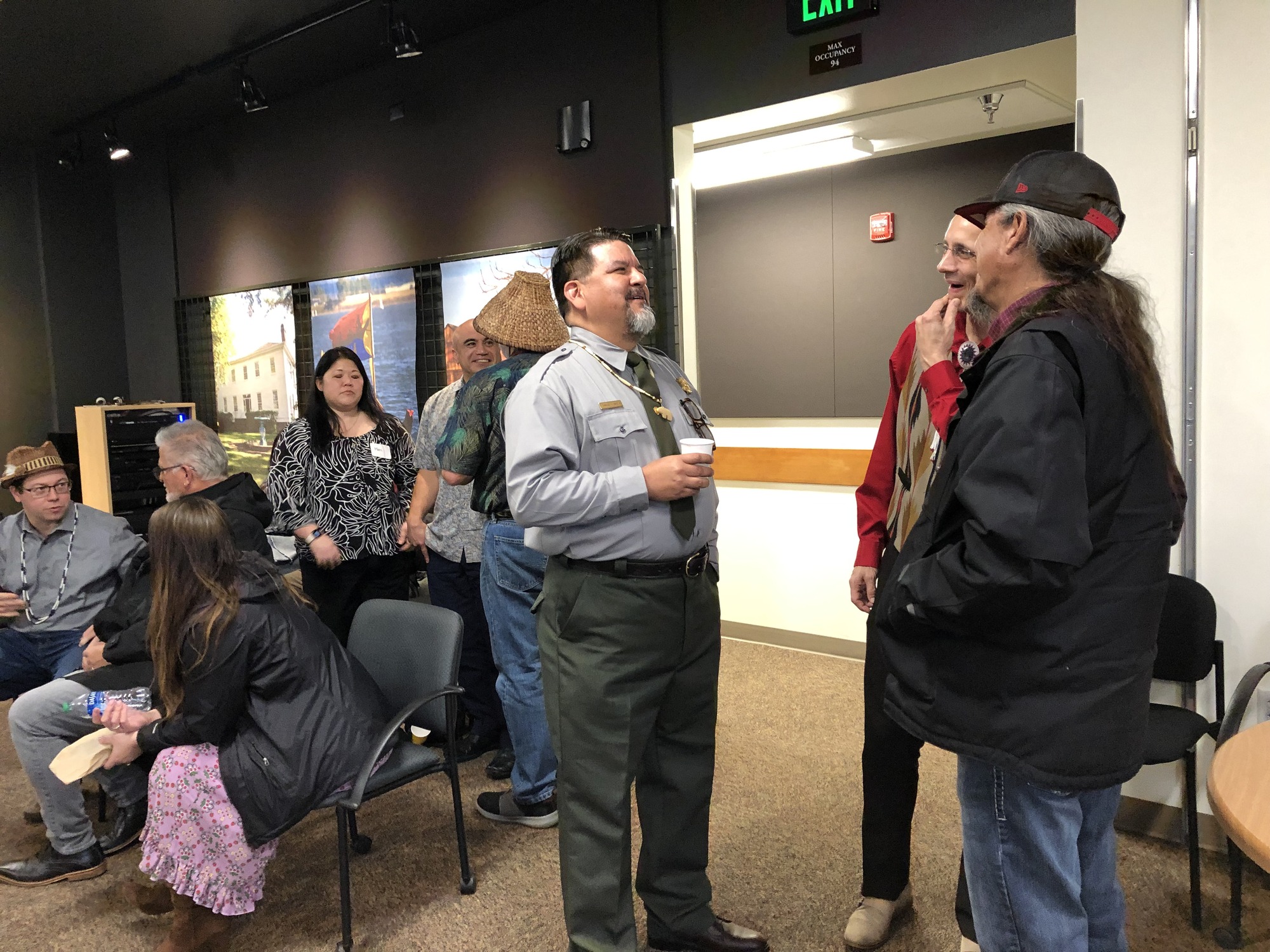 A man wearing a National Park Service uniform talks to two other men inside a theater space.