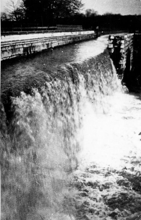 B&W photo of water gushing over high stone aqueduct