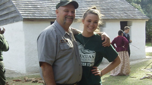 volunteer in green shirt smiles with ranger who has arm around her