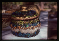 A small basked adorned with blue, grey, brown, and green feathers.