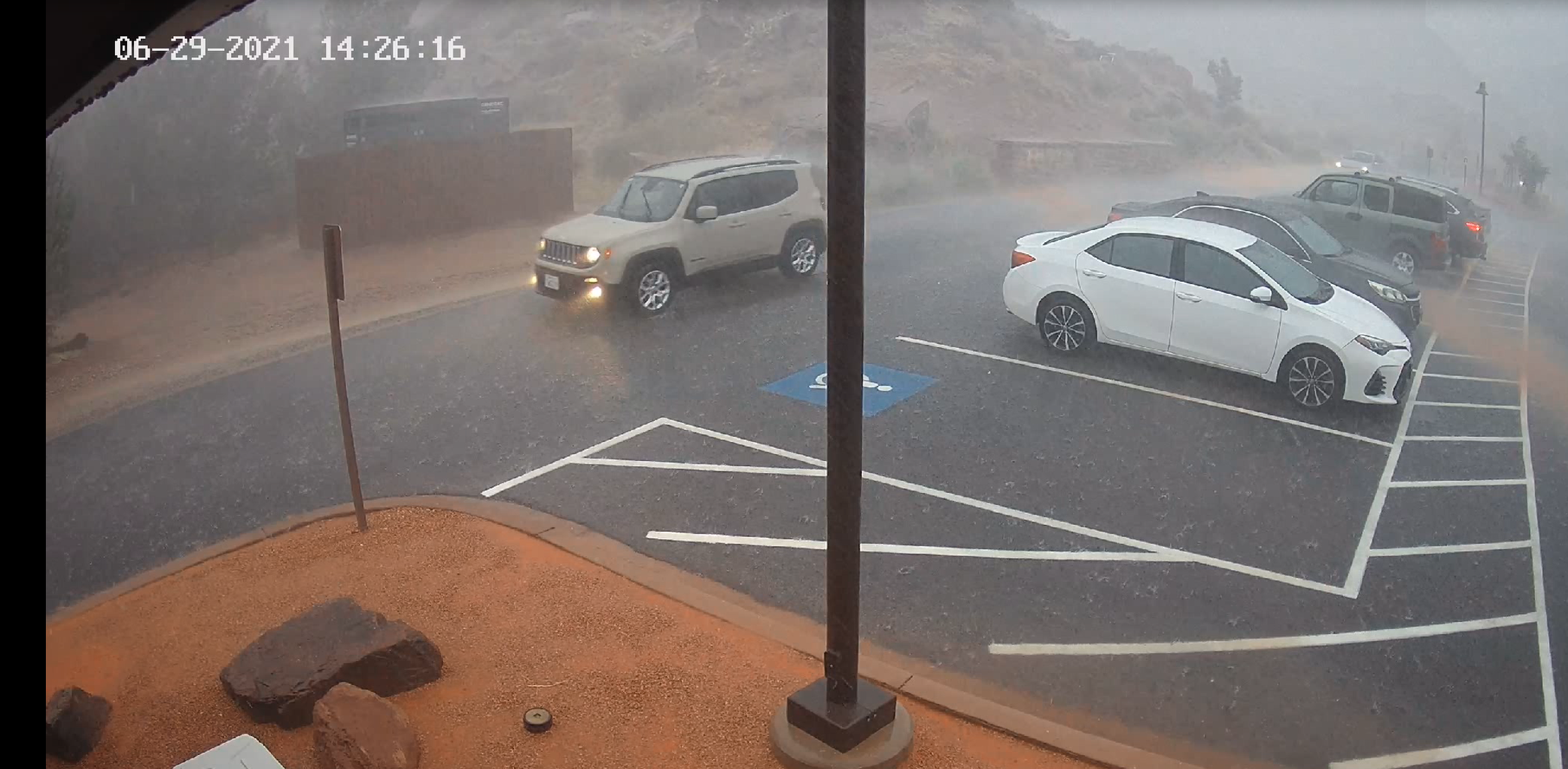 A white car drives through heavy rain towards the exit of the park. 