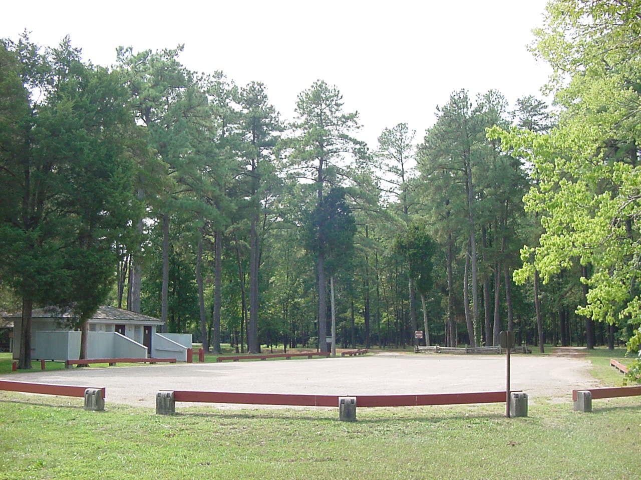 Paved parking lot with horizontal wooden poles to mark boundary. One man, one woman, and one family restroom to the left.