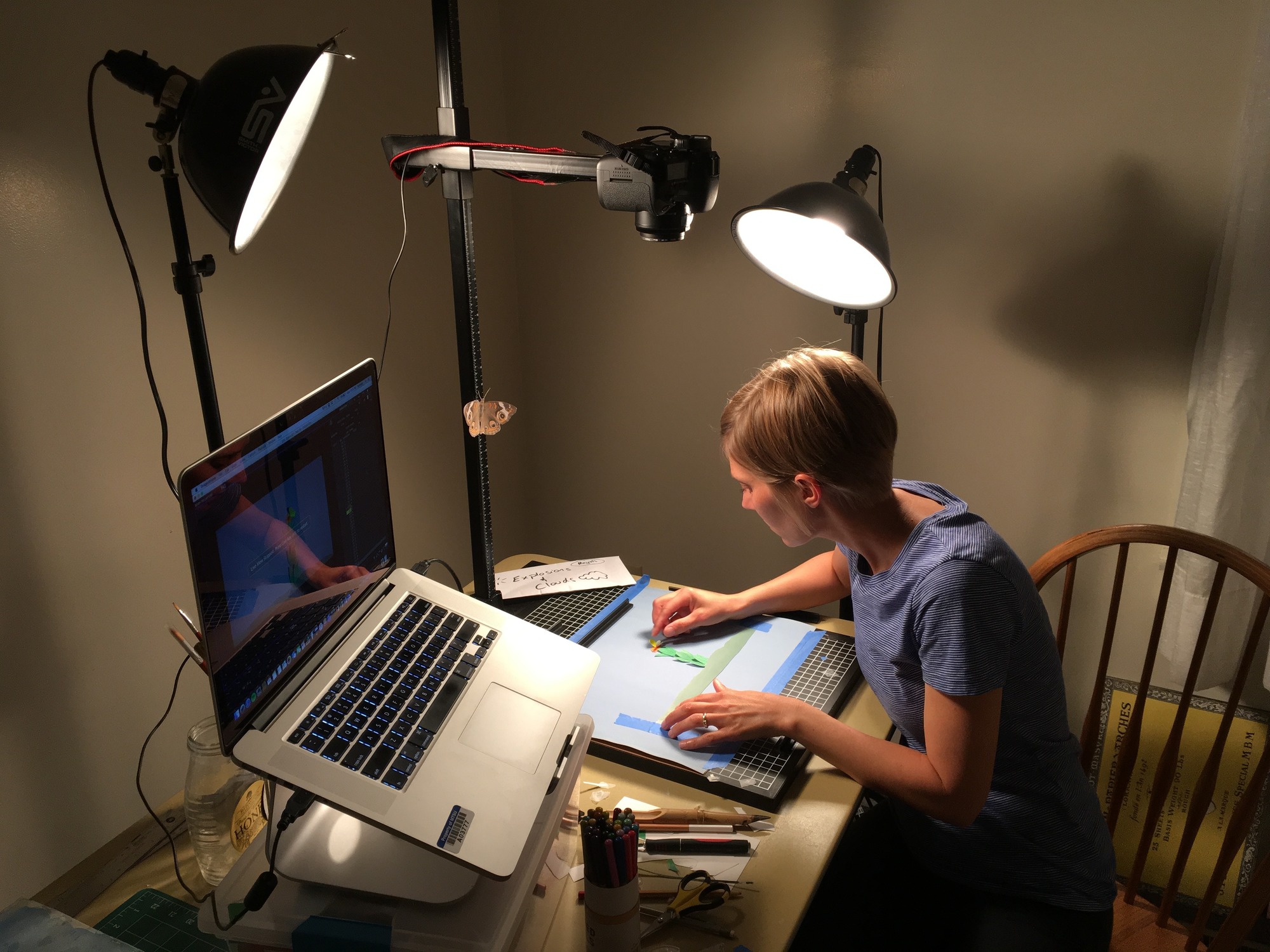 A woman works on artwork at a table with a computer.