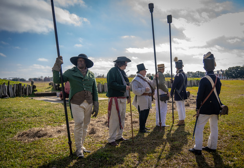 Six men in period clothing stand together outside.