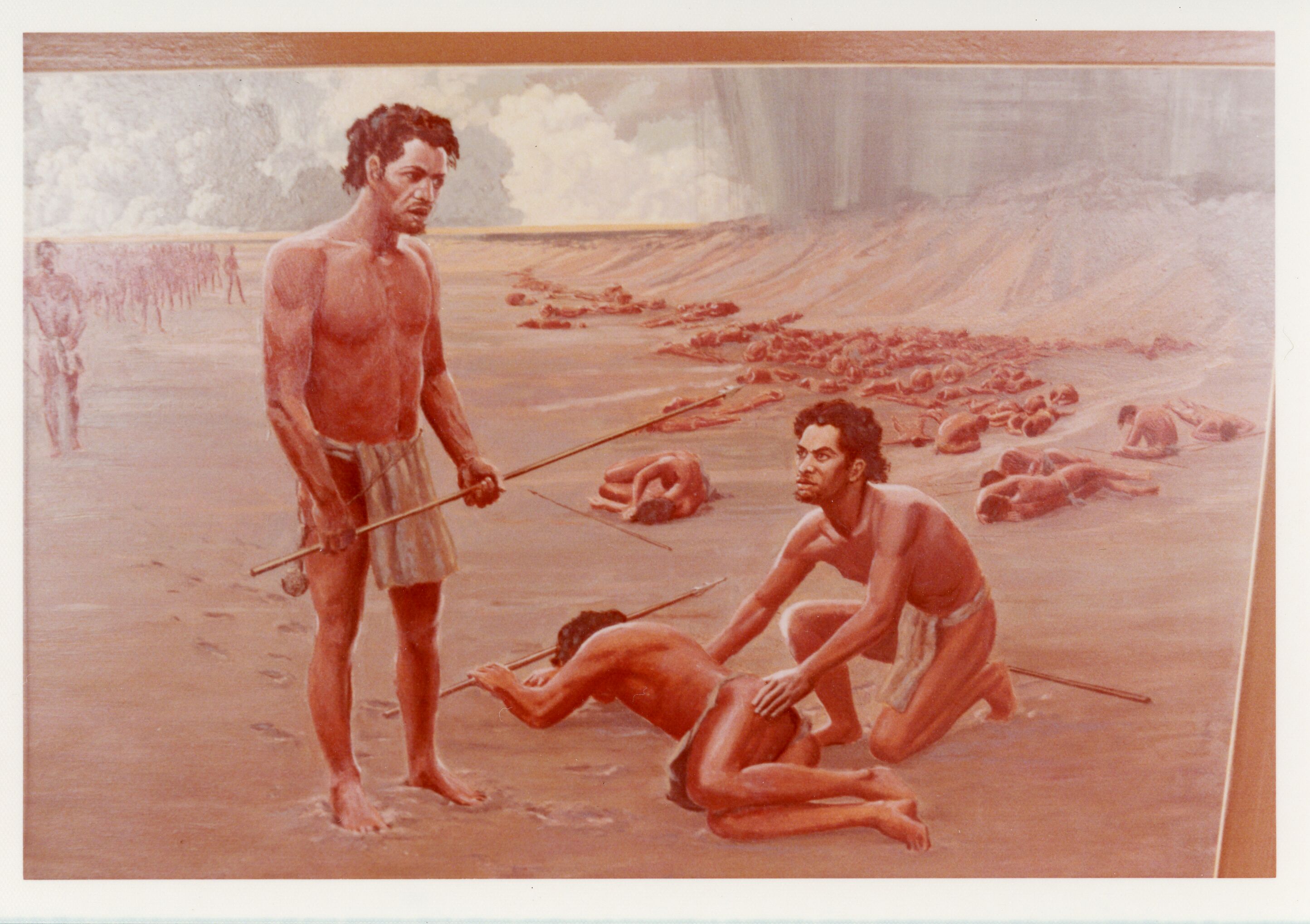 A colored image of people after a battle. Towards the left side of the image there is a man standing holding onto a wooden spear. He is wearing a loin cloth. He has brown curly hair, a short beard, and tan skin. To the right of him is a man lying on the ground with his head turned down in the sand. He is holding onto a wooden spear in his left hand. He has tan skin with brown hair and is wearing a loin cloth. Next to him is a man kneeling down on one knee. His left hand is on the injured man's buttocks and his right hand is on the injured man's right shoulder. He has tan skin, brown curly hair, and is wearing a loin cloth. His spear is located behind him. In the background there are other people in a variety of poses, some of them are sitting or lying down. Beyond the injured is the slope of the coastline. There is gray ash falling from the sky onto the slope. In the far-left background of the image there is a shadow of a group of people walking towards the injured.