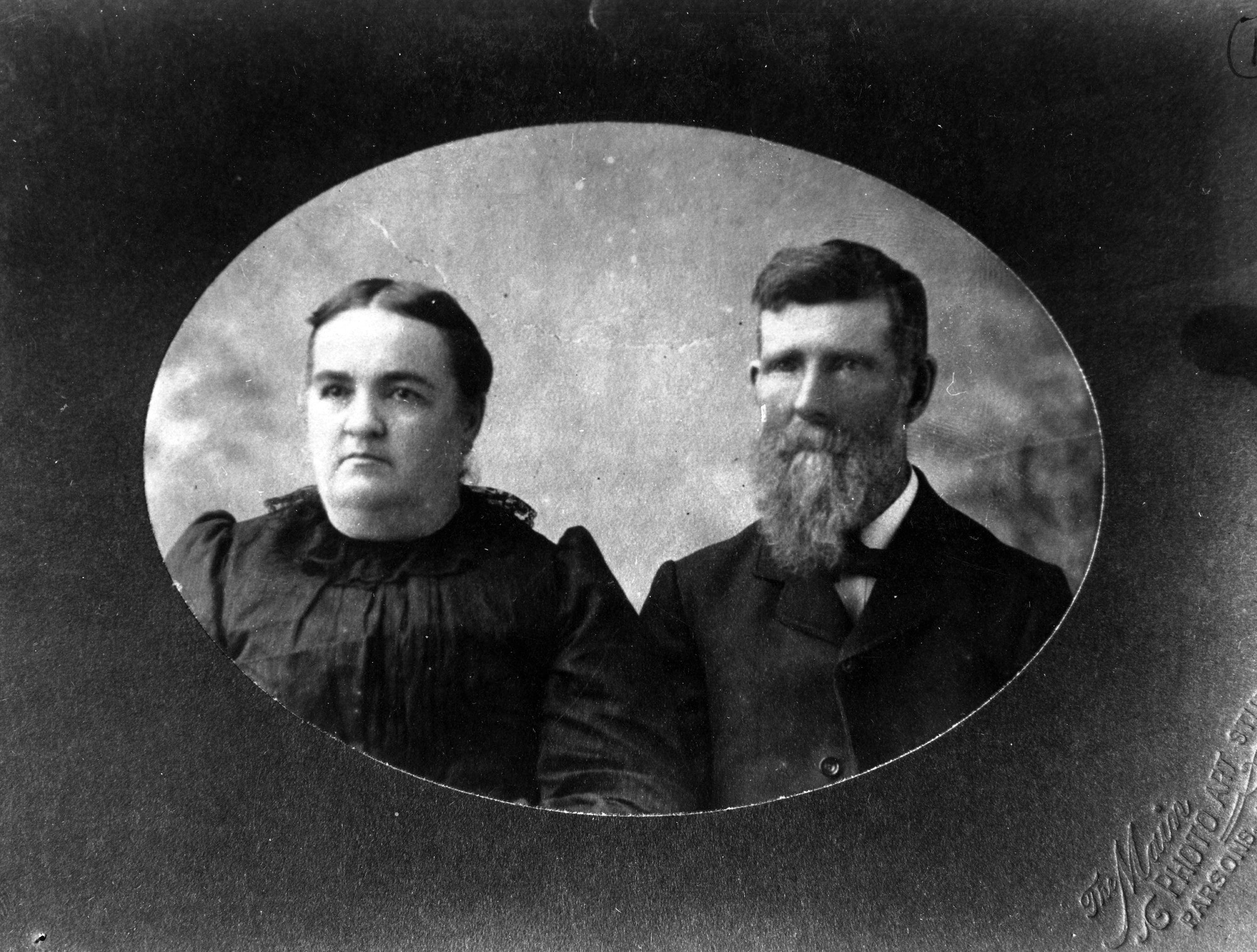 A framed portrait photo depicts a plump woman and bearded man in 1880s dress.