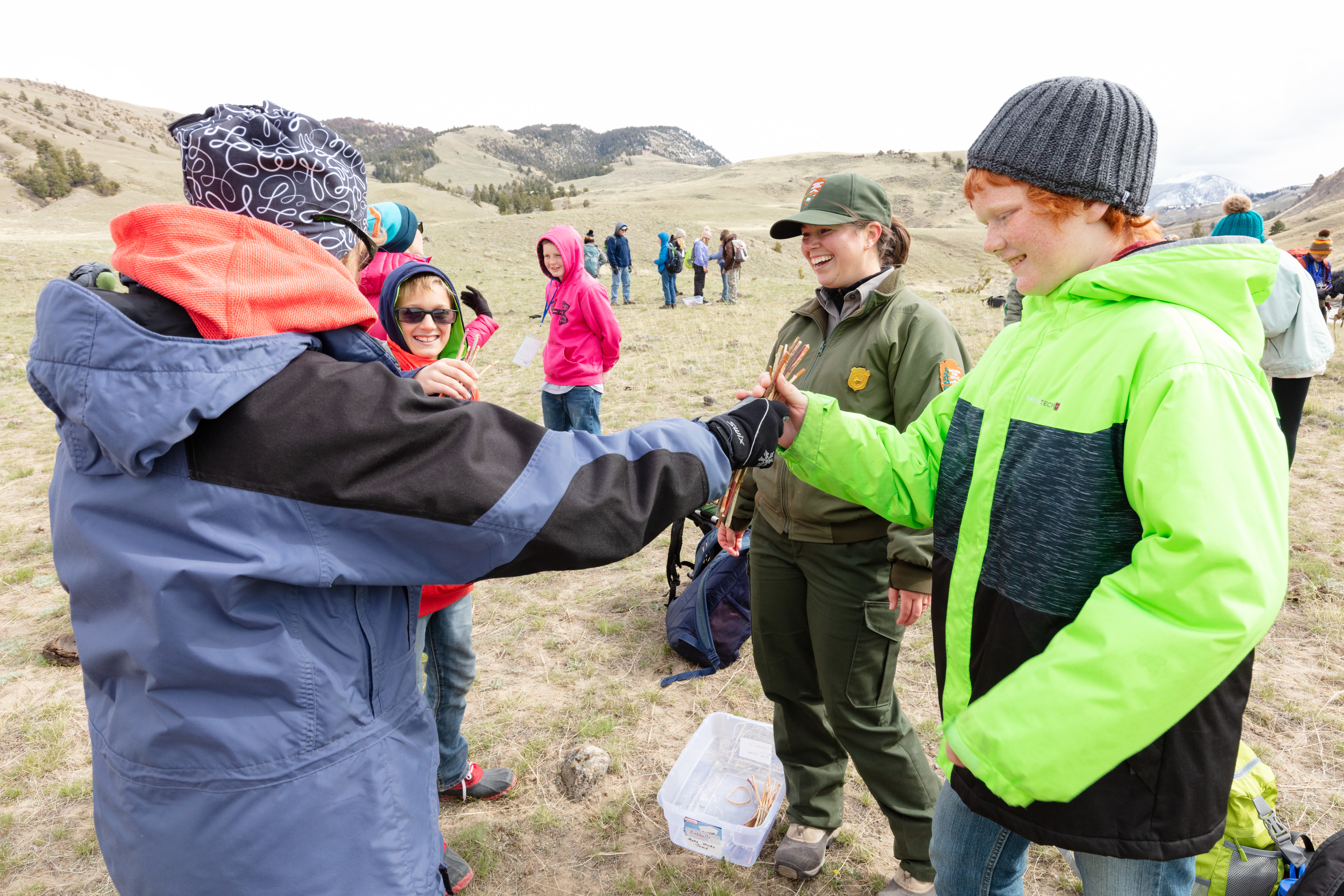 A ranger talks with young people as two of them trade a handful of sticks