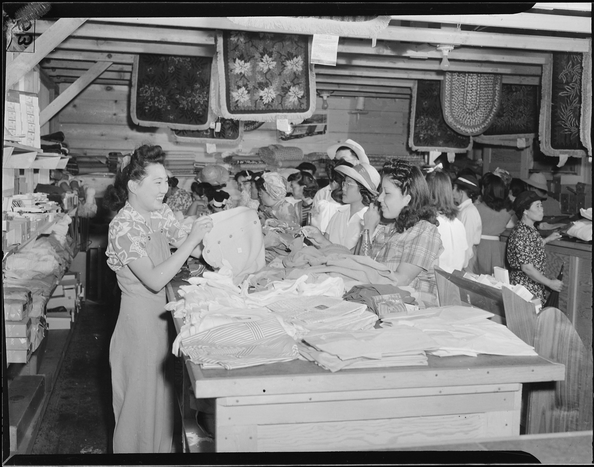 Lillian Hiraike, 18, evacuee from Seattle, Washington, shows a sweater to a prospective buyer in the general store at this War Relocation Authority center for evacuees of Japanese ancestry