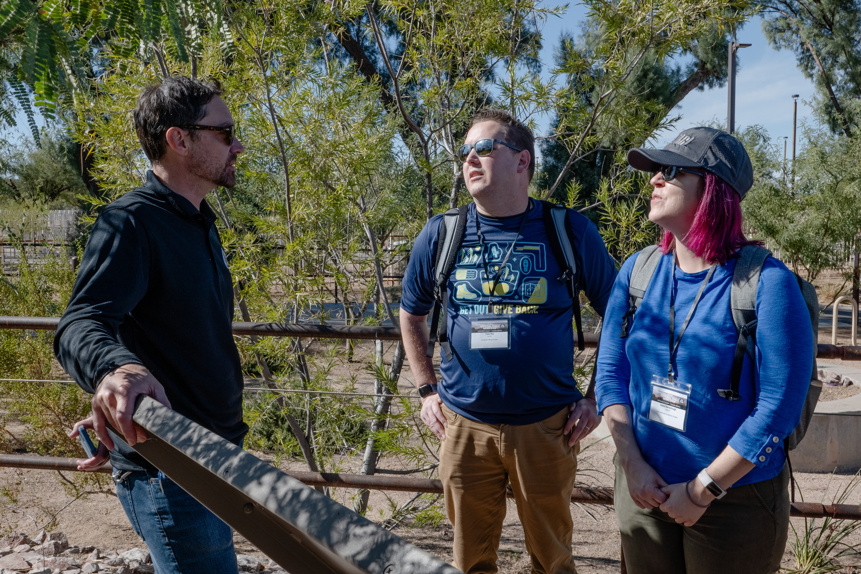 Three people talk to each other in front of a wayside at the park