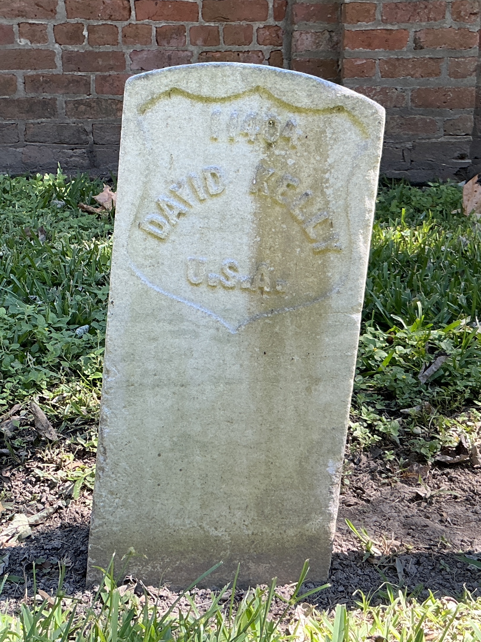 Front of historic upright marble headstone with recessed shield with recessed lettering face.