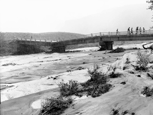 Partial collapse of Coal pits Wash bridge on State Route 15 (now State Route 9). Image shows several people viewing the damage and debris of the 'Great Flood of September' which claimed the lives of 5 persons in the Narrows on September 17, 1961. The flood waters have receded considerably and show the flotsam and destruction caused by the floods on the Virgin River. [See ZION 8598 , ZION 8600, and ZION 8601.]