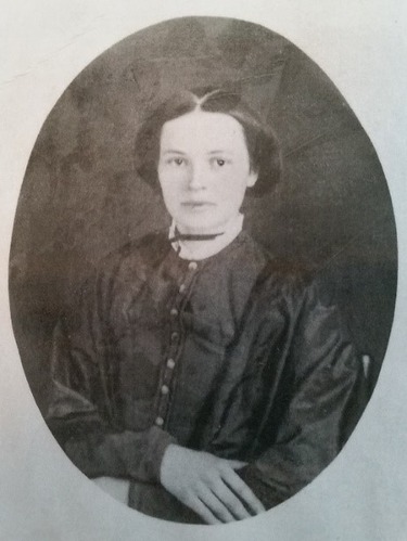 a young woman with short dark hair. She is sitting with her hands folded on her lap.