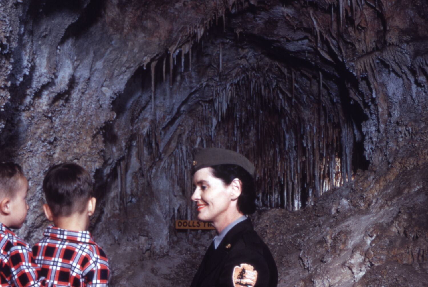 Woman in uniform talking to two small boys while standing in a cavern.