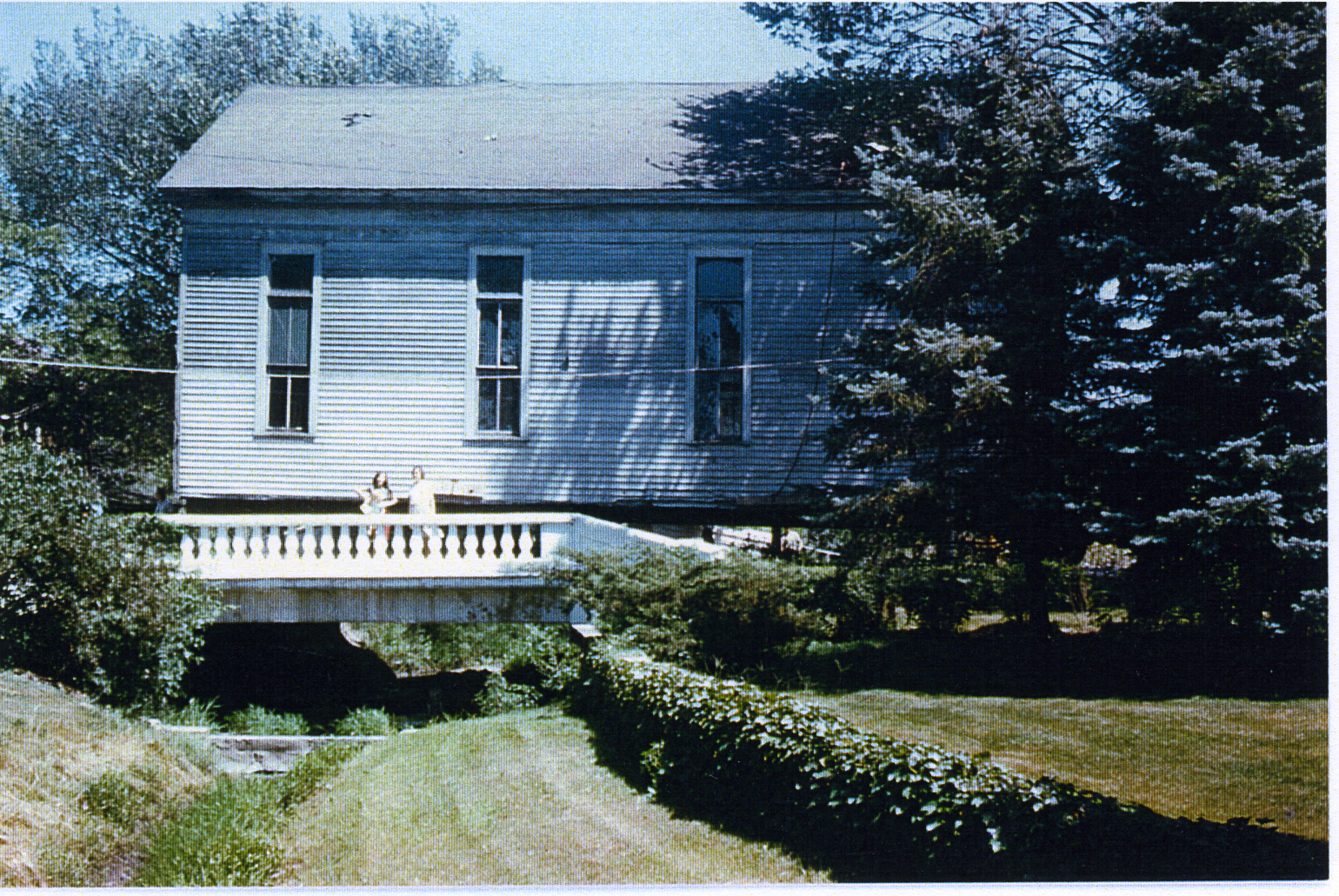 Two young women pose on a small concrete rural bridge as a building being moved crosses it.