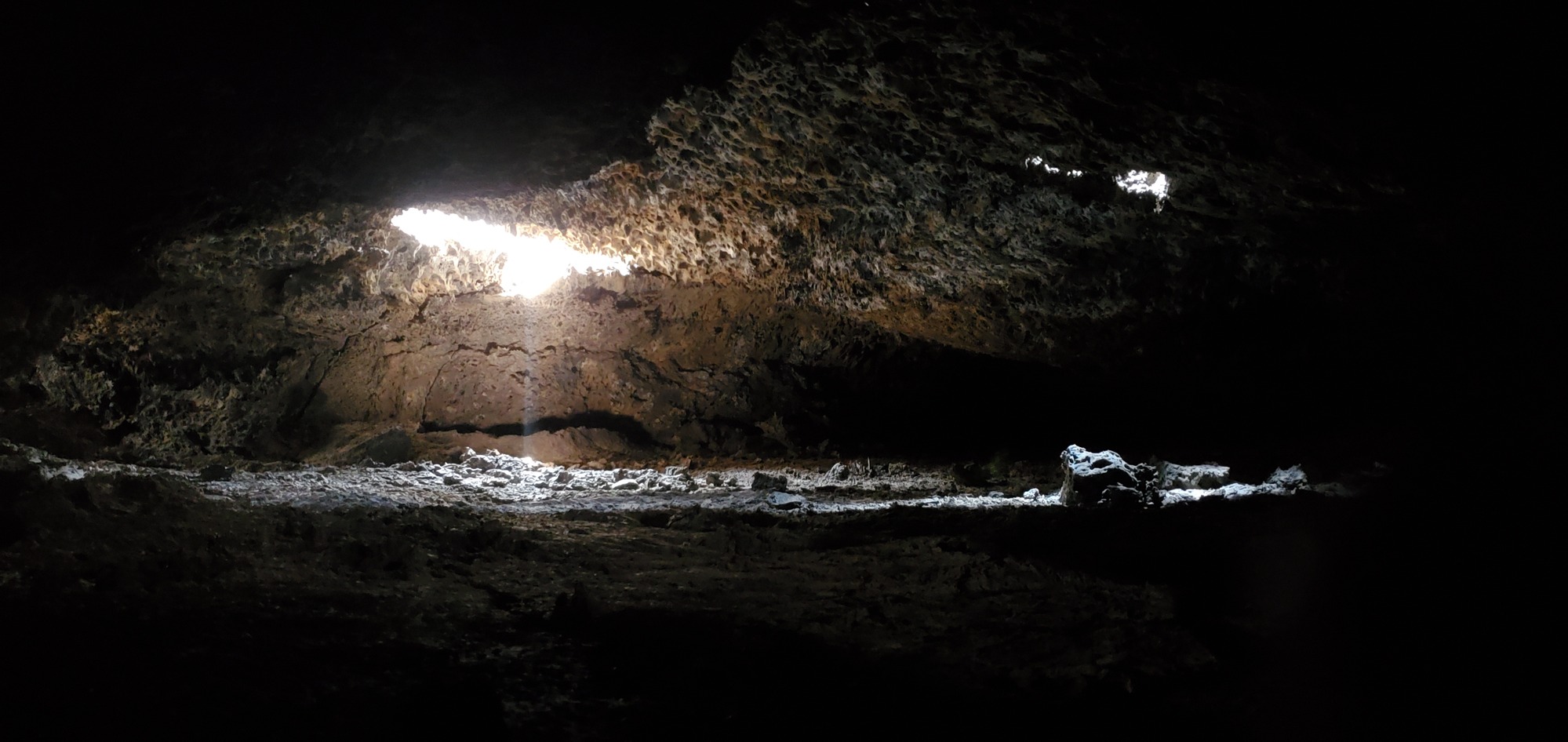 light illuminating part of a wide cave passage from the ceiling which is covered with small lava stalactites