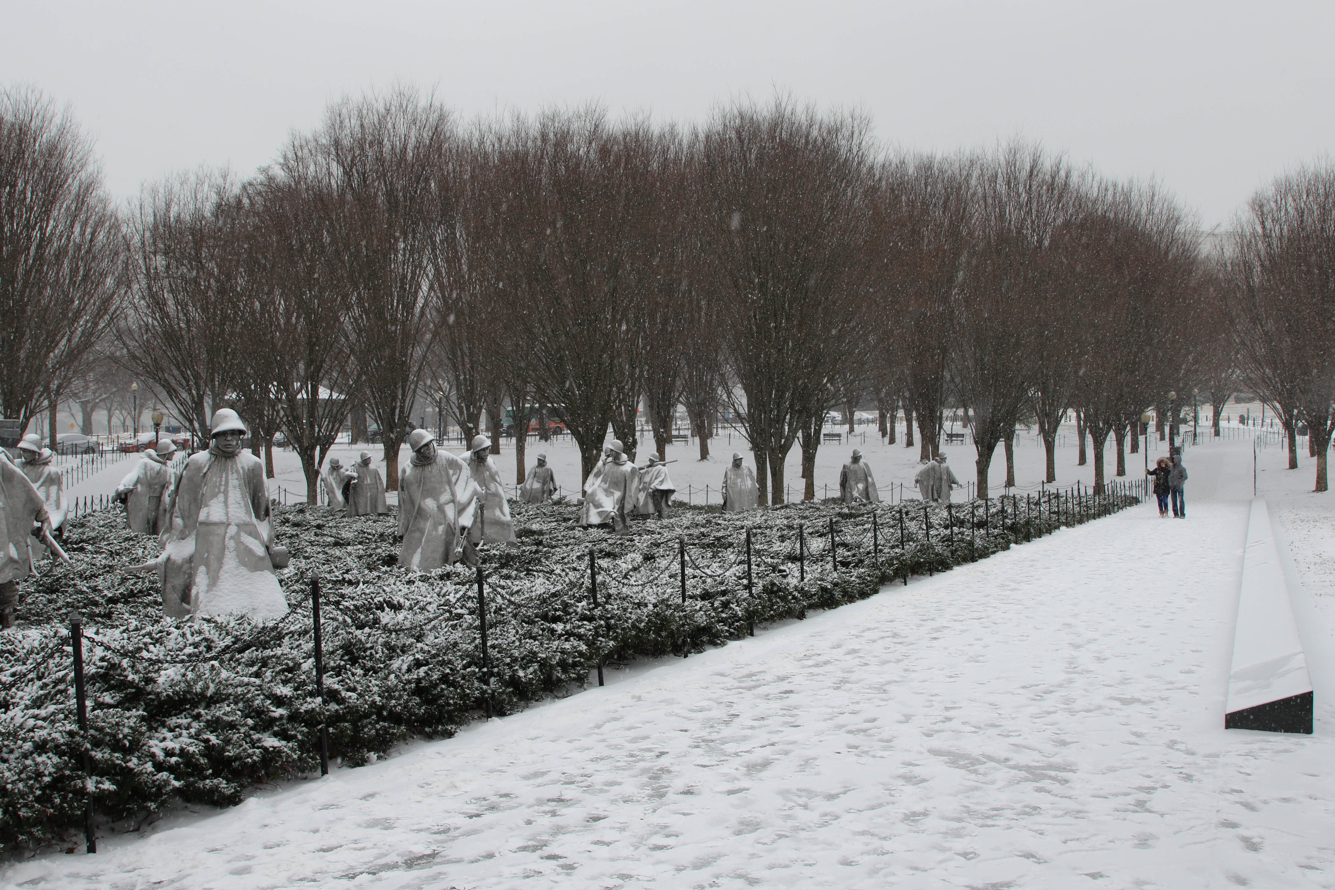 Visitors on snow-covered walkway next to statues of American servicemen