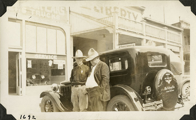 This is an historic black and white photograph from the Scotty's Castle Historic Photograph Collection, Death Valley National Park of Albert M. Johnson and Walter Edward Perry Scott, in front of an automobile sales service store and a Dodge Victory 6 sedan, probably in Tonopah, Nevada. Circa 1928.