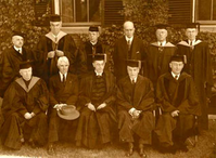 Sepia toned photograph of 11 men, five seated in front, 6 standing in rear.  All are in doctoral robes with the exception of one , Carl Sandburg, who has a hat on his lap.