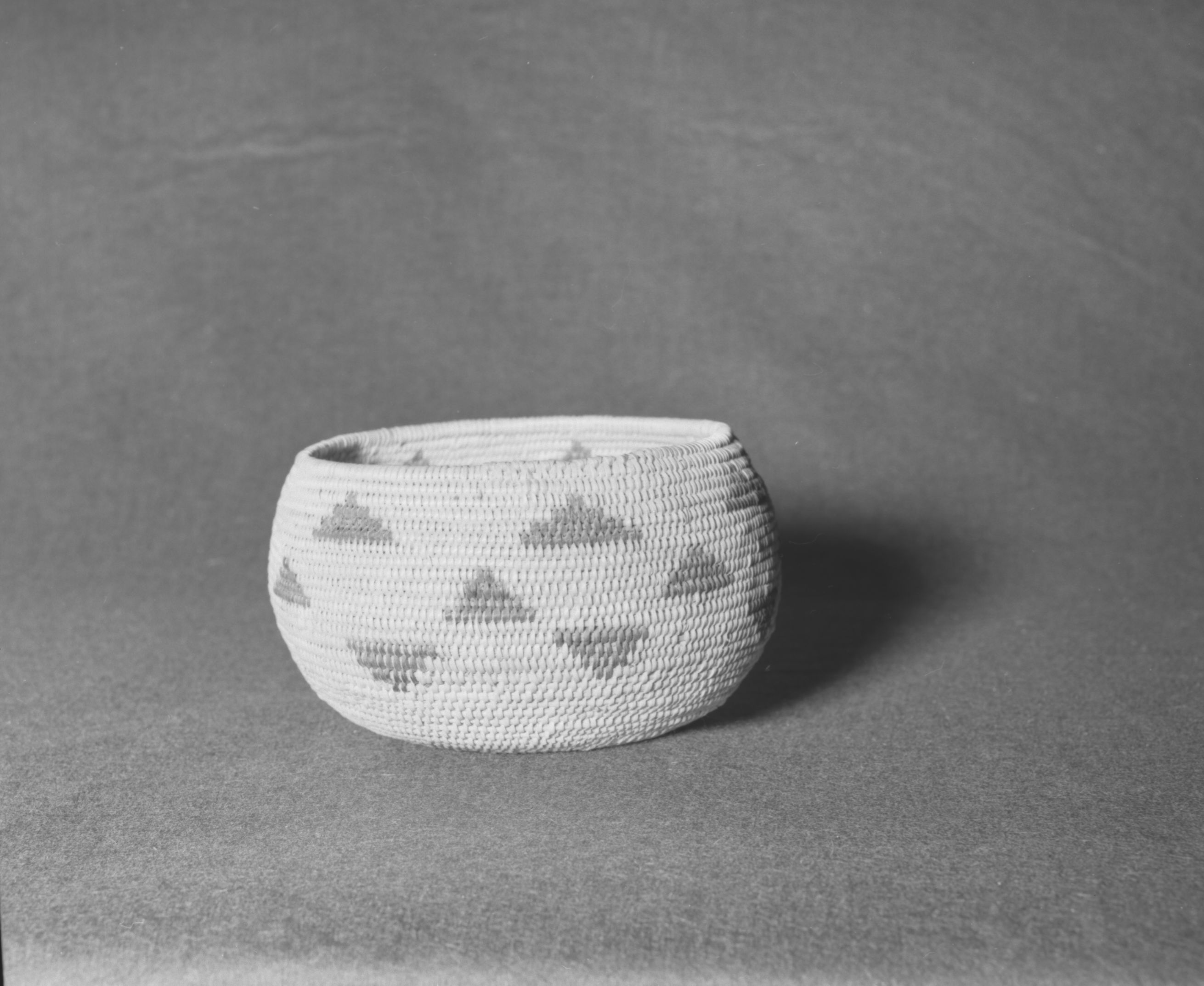 Mrs. Geraldine McConnell Collection. Object: Miwok basket, made at Murphys, Calaveras Co., c. 1900-1910. Dimensions: 6" x 3 1/2". Materials: Bracken fern root pattern, background of split shoots, possibly big leaf maple. Technology: Three-rod, clockspring start filled with stitches, interlocking stitch, fag ends trimmed on work face, moving ends trimmed on interior. Photographed by Michael Dixon in January 1983. Catalogued by Craig Bates and Barbara Beroza. Yosemite Collections, National Park Service.