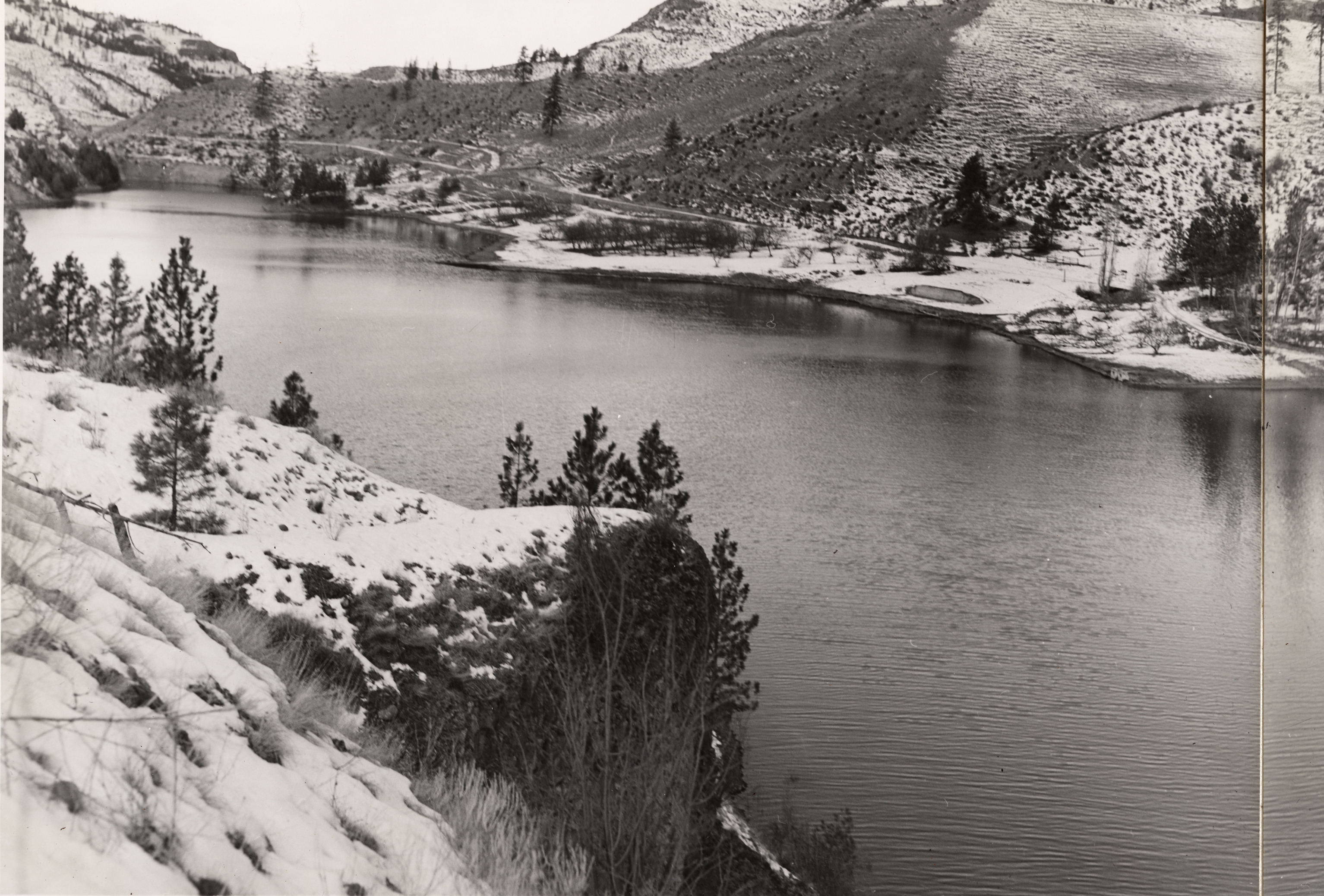 Black and white photograph of a steep, snowy cliff next to a body of water