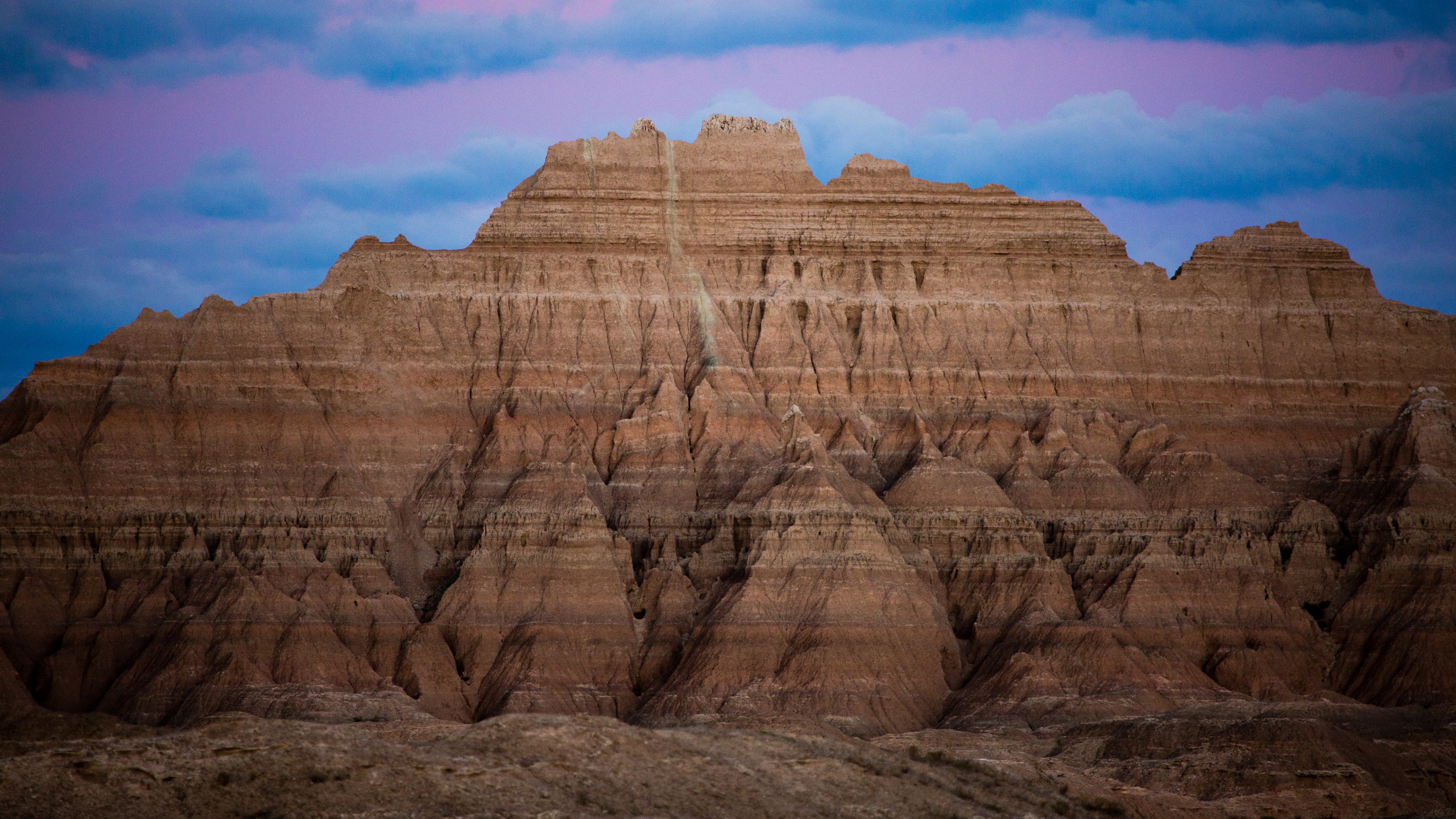A tall ridge line and many rock hoodoos rise above the plains at Badlands National Park just after sunset.